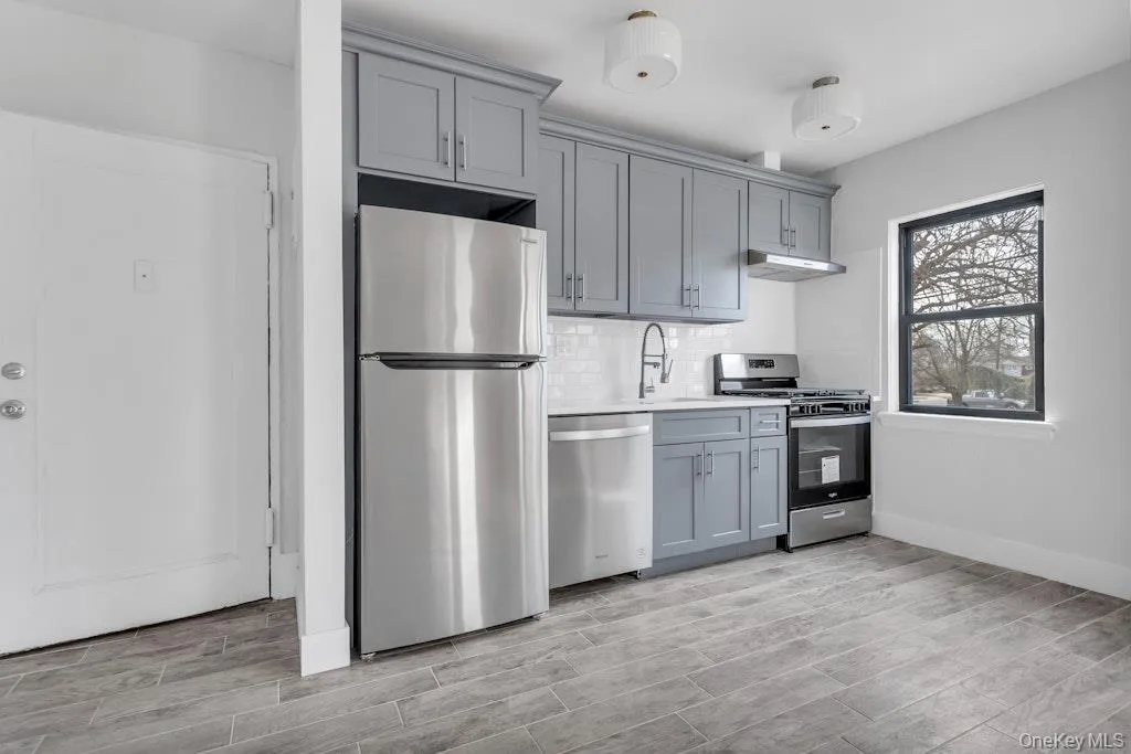 Kitchen with tasteful backsplash, stainless steel appliances, gray cabinetry, under cabinet range hood, and a sink Kitchen with tasteful backsplash, stainless steel appliances, gray cabinetry, under cabinet range hood, and a sink