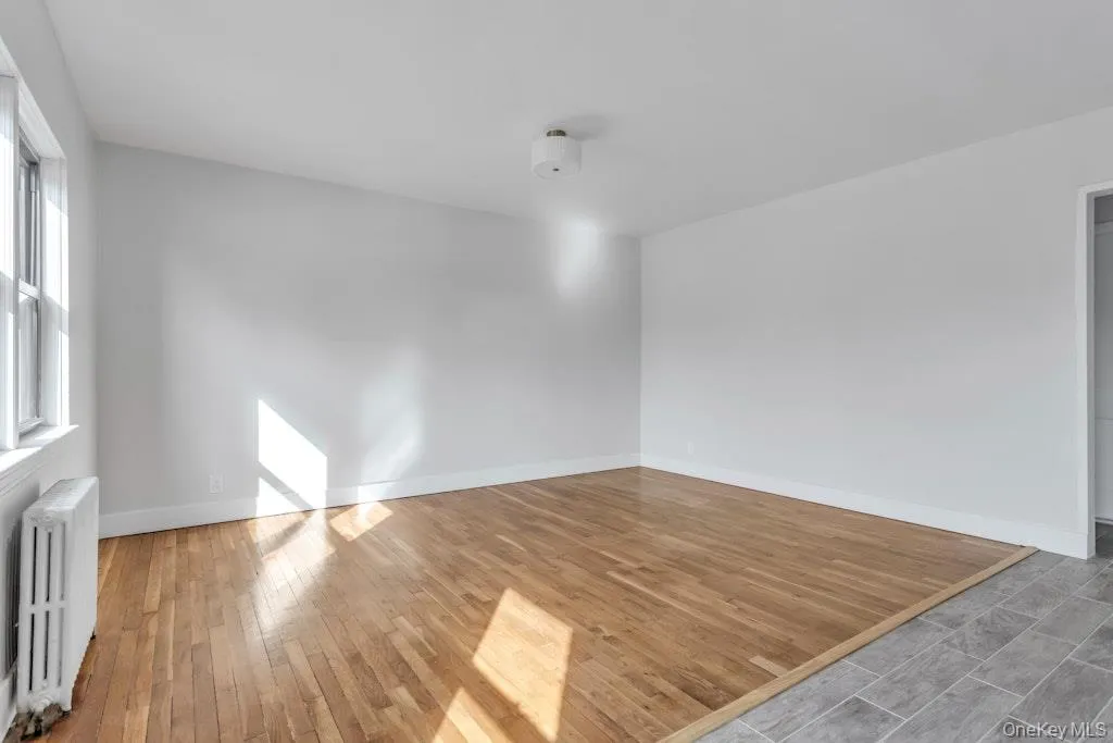 Empty room featuring wood-type flooring, baseboards, and radiator heating unit Empty room featuring wood-type flooring, baseboards, and radiator heating unit
