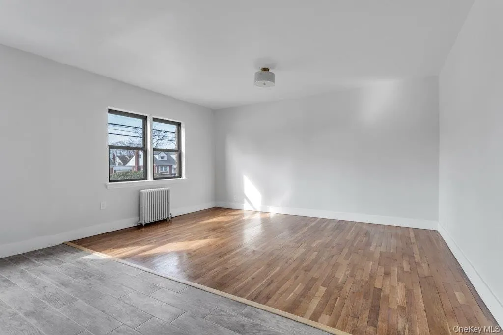Spare room featuring radiator heating unit, wood finished floors, and baseboards Spare room featuring radiator heating unit, wood finished floors, and baseboards