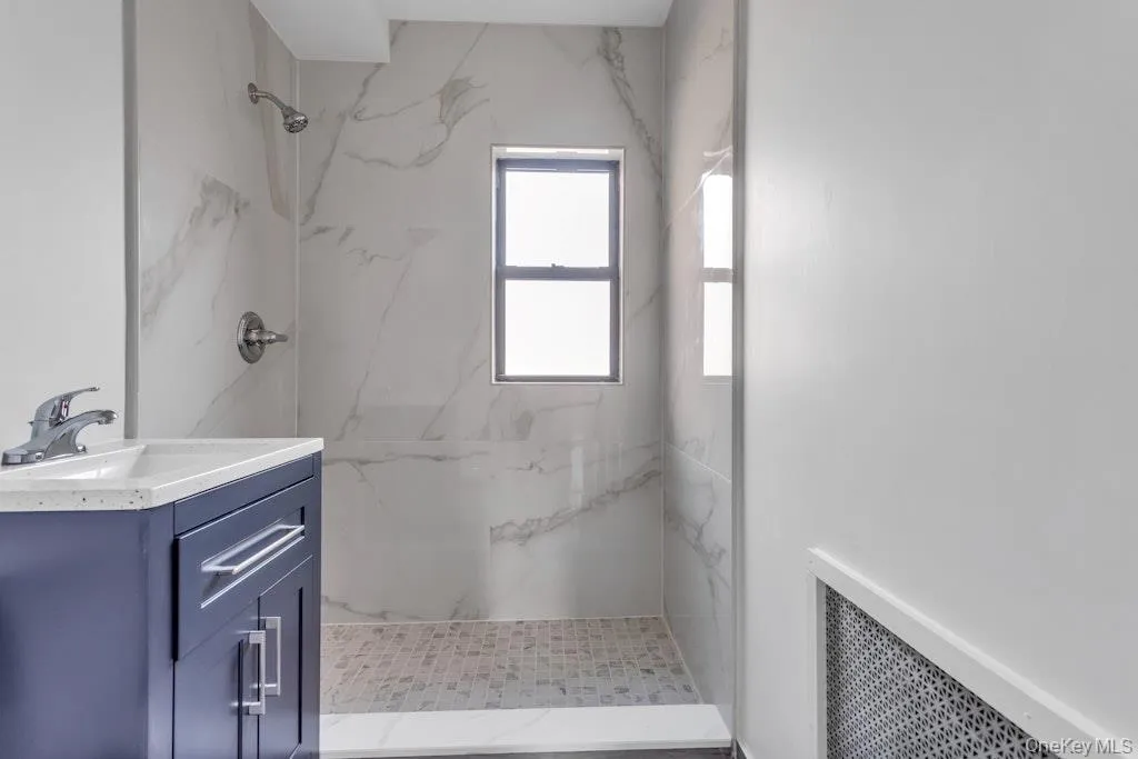 Full bathroom with radiator heating unit, vanity, and a marble finish shower Full bathroom with radiator heating unit, vanity, and a marble finish shower