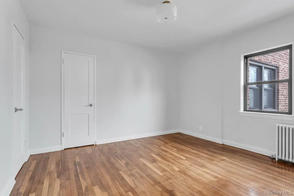 Empty room with radiator heating unit, light wood-type flooring, and baseboards Empty room with radiator heating unit, light wood-type flooring, and baseboards