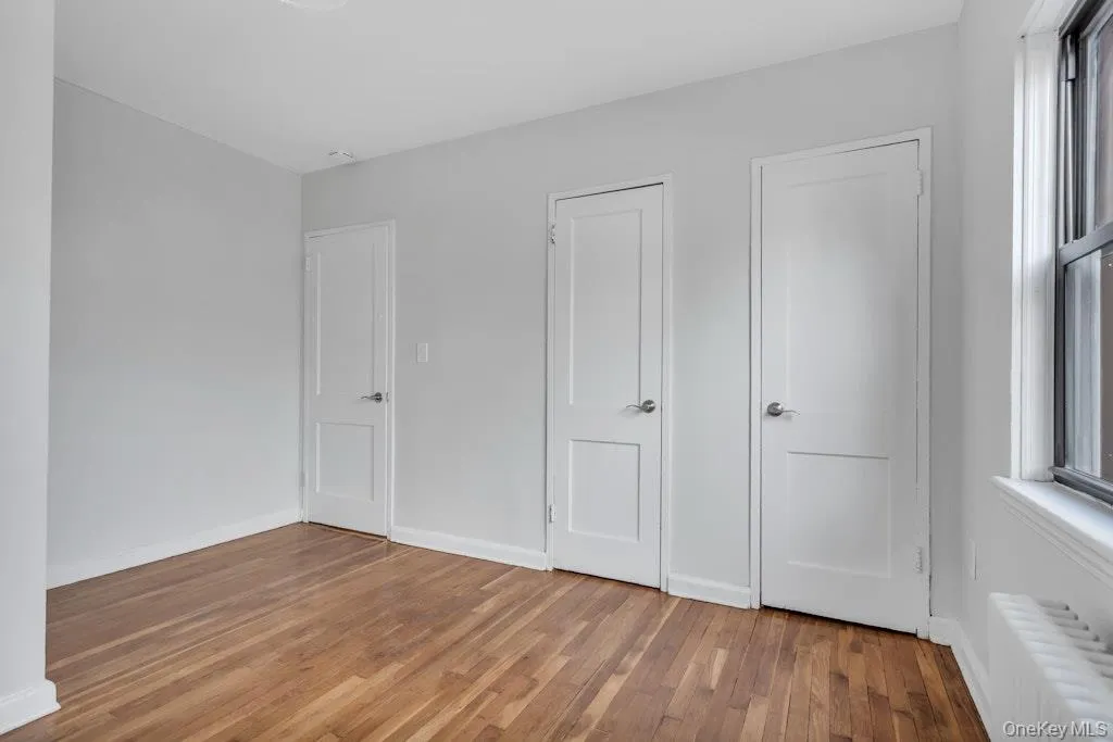 Unfurnished bedroom with light wood-style floors, radiator heating unit, multiple windows, and baseboards Unfurnished bedroom with light wood-style floors, radiator heating unit, multiple windows, and baseboards