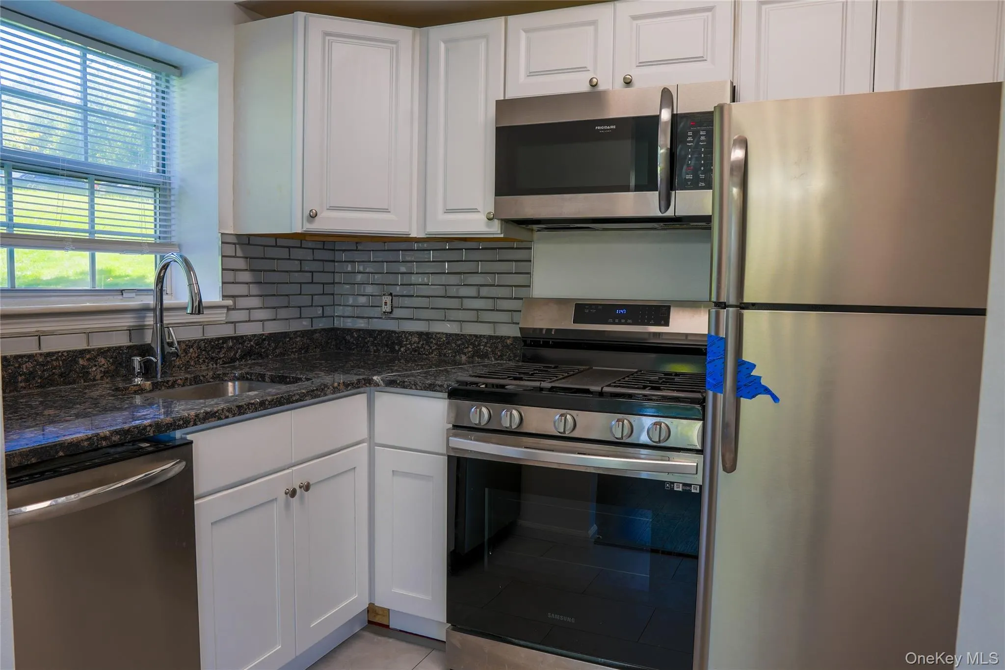 Kitchen with white cabinetry, dark stone countertops, stainless steel appliances, and a gray subway tile backsplash Kitchen with white cabinetry, dark stone countertops, stainless steel appliances, and a gray subway tile backsplash