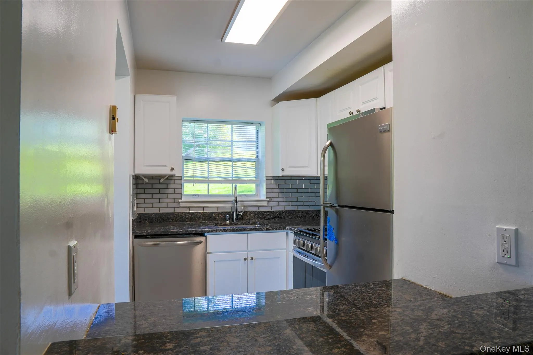 Kitchen featuring dark stone countertops, white cabinetry, a rectangular stainless steel sink with a gooseneck faucet, a tile backsplash, and stainless steel appliances Kitchen featuring dark stone countertops, white cabinetry, a rectangular stainless steel sink with a gooseneck faucet, a tile backsplash, and stainless steel appliances