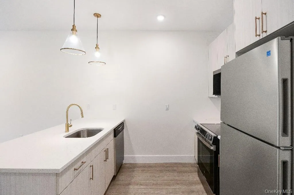 Kitchen with sink, light hardwood / wood-style floors, decorative light fixtures, and appliances with stainless steel finishes Kitchen with sink, light hardwood / wood-style floors, decorative light fixtures, and appliances with stainless steel finishes