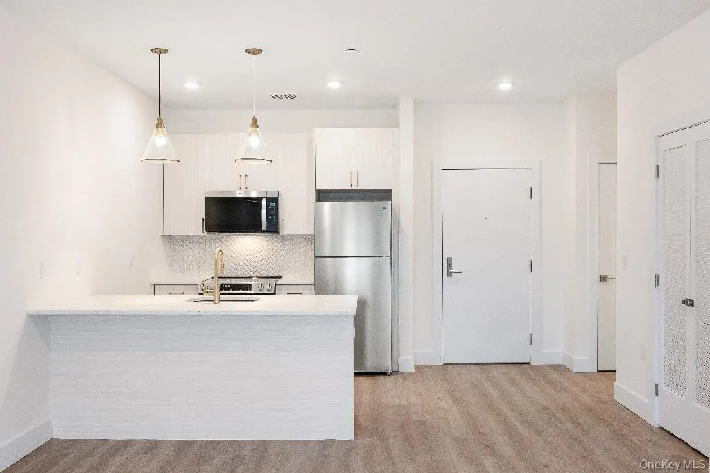 Kitchen with backsplash, hanging light fixtures, appliances with stainless steel finishes, light hardwood / wood-style floors, and white cabinetry Kitchen with backsplash, hanging light fixtures, appliances with stainless steel finishes, light hardwood / wood-style floors, and white cabinetry
