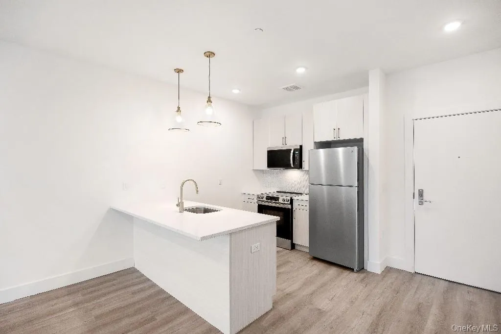 Kitchen featuring backsplash, stainless steel appliances, sink, decorative light fixtures, and white cabinetry Kitchen featuring backsplash, stainless steel appliances, sink, decorative light fixtures, and white cabinetry