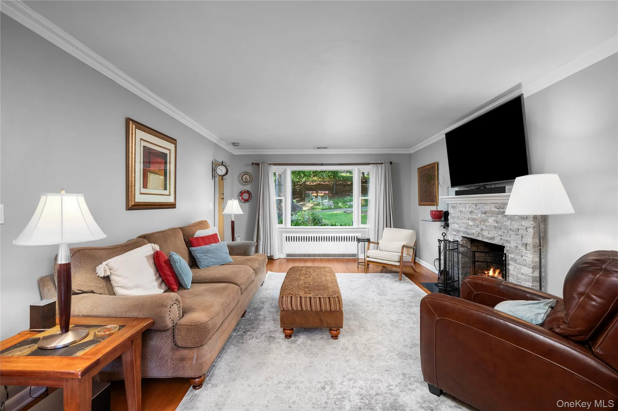 A warm and inviting living room featuring rich hardwood floors, a wood-burning fireplace, and large windows that fill the space with natural light A warm and inviting living room featuring rich hardwood floors, a wood-burning fireplace, and large windows that fill the space with natural light