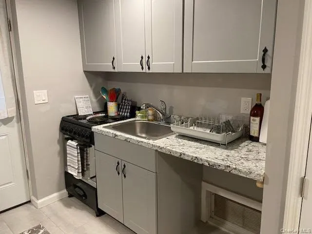 Kitchen with gray cabinets, light stone counters, light tile patterned floors, and black range Kitchen with gray cabinets, light stone counters, light tile patterned floors, and black range