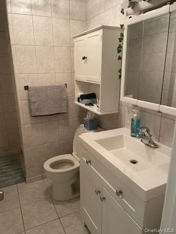 Bathroom with tile walls, vanity, light tile patterned floors, and a shower stall Bathroom with tile walls, vanity, light tile patterned floors, and a shower stall