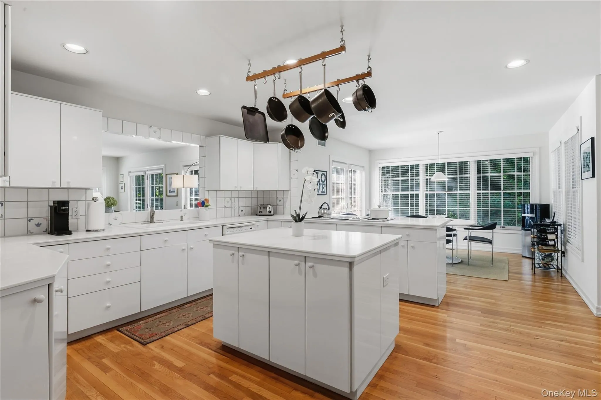 Cooks' kitchen with white, tiled backsplash and Corian countertops overlooking the family room, double white enamel sink, center island with electrical outlet and storage beneath, dining area, entry to family room and doors out to deck Cooks' kitchen with white, tiled backsplash and Corian countertops overlooking the family room, double white enamel sink, center island with electrical outlet and storage beneath, dining area, entry to family room and doors out to deck