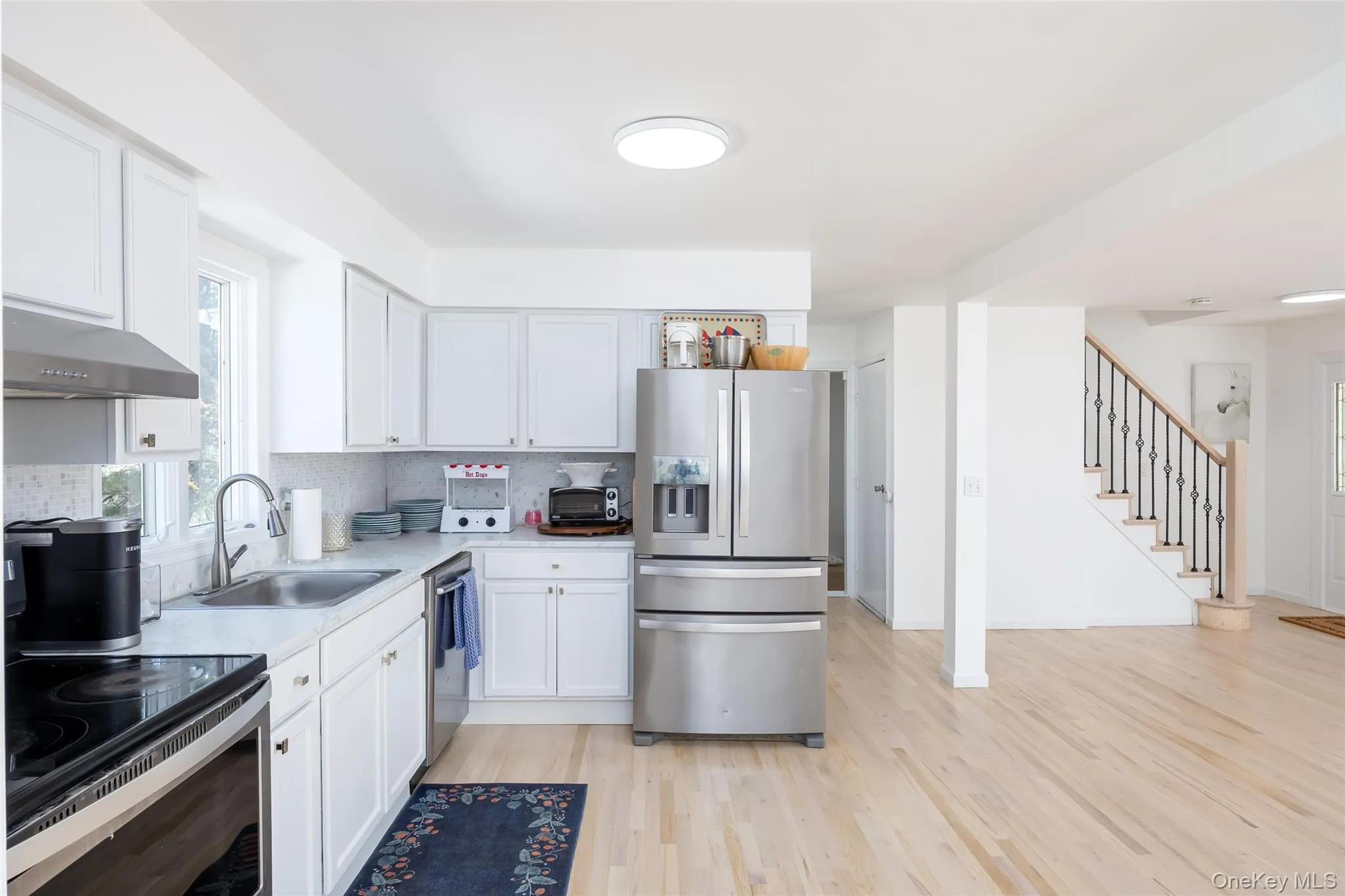 Kitchen featuring appliances with stainless steel finishes, a sink, under cabinet range hood, light countertops, and light wood-style flooring Kitchen featuring appliances with stainless steel finishes, a sink, under cabinet range hood, light countertops, and light wood-style flooring