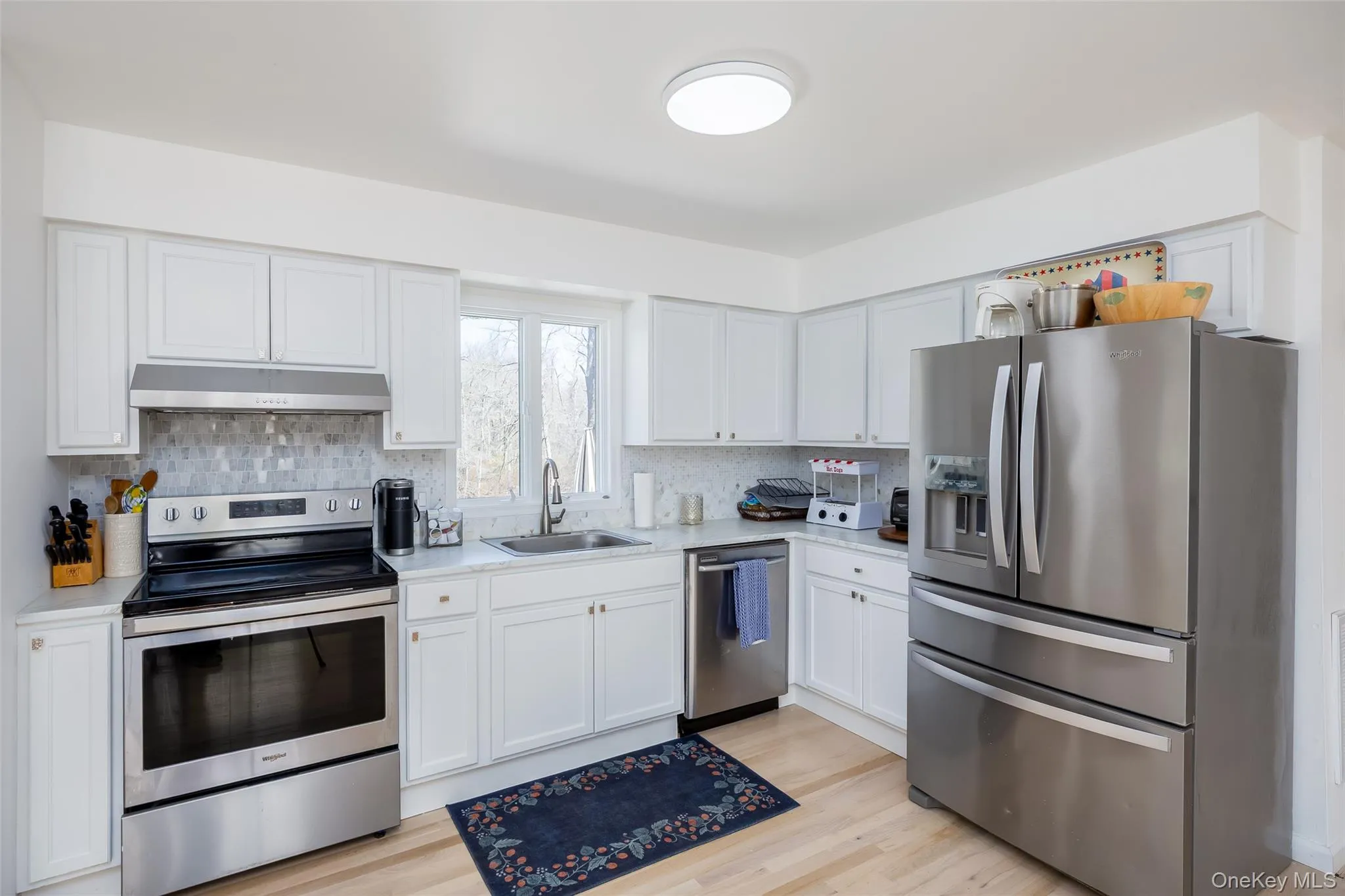Kitchen featuring stainless steel appliances, under cabinet range hood, a sink, and light countertops Kitchen featuring stainless steel appliances, under cabinet range hood, a sink, and light countertops