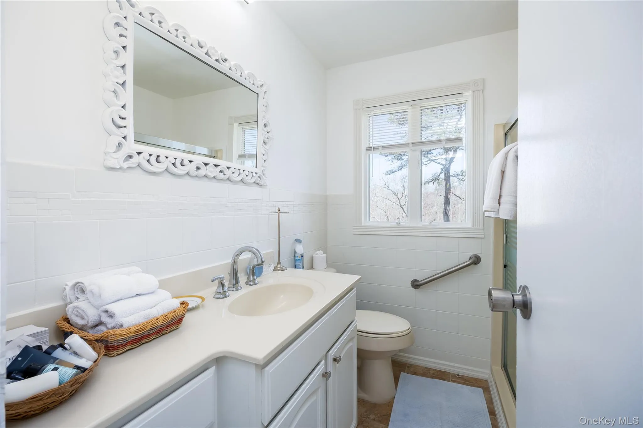 Full bath featuring tile walls, toilet, vanity, and wainscoting Full bath featuring tile walls, toilet, vanity, and wainscoting