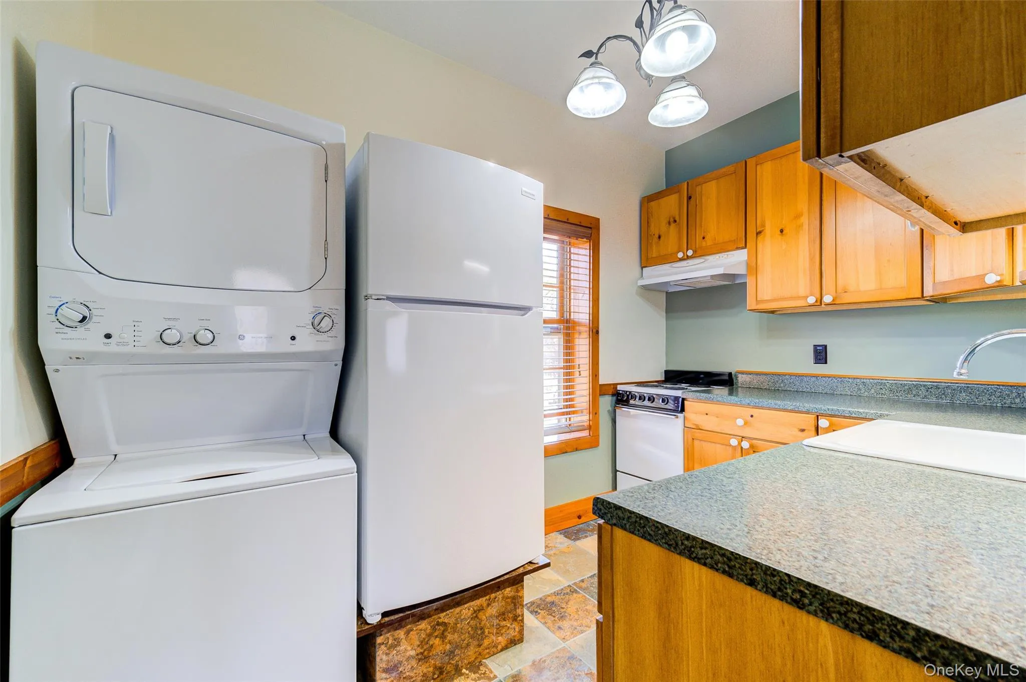 Kitchen featuring white appliances, sink, decorative light fixtures, a notable chandelier, and stacked washer / dryer Kitchen featuring white appliances, sink, decorative light fixtures, a notable chandelier, and stacked washer / dryer