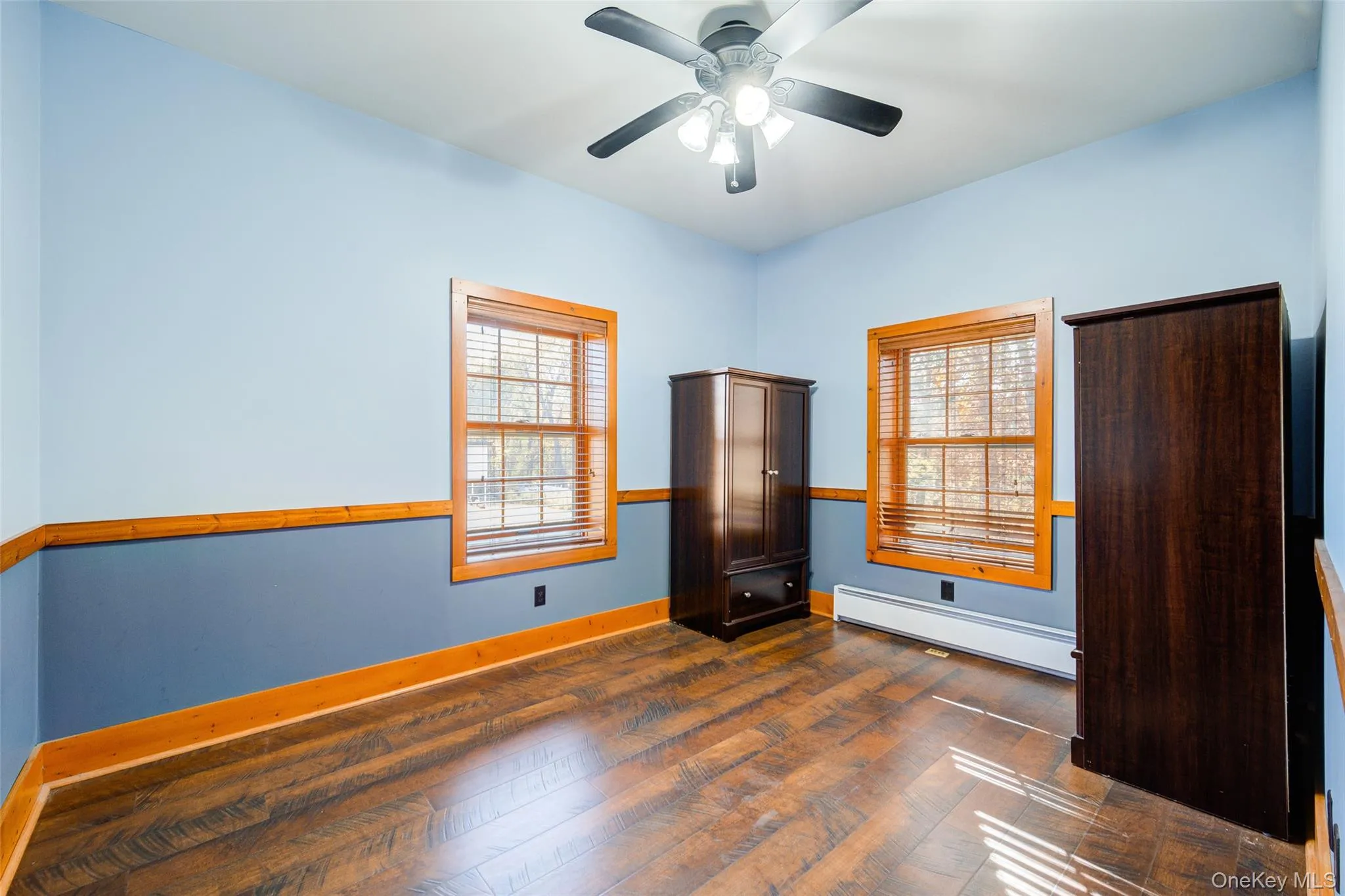 Empty room with dark hardwood / wood-style floors, ceiling fan, and a baseboard heating unit Empty room with dark hardwood / wood-style floors, ceiling fan, and a baseboard heating unit