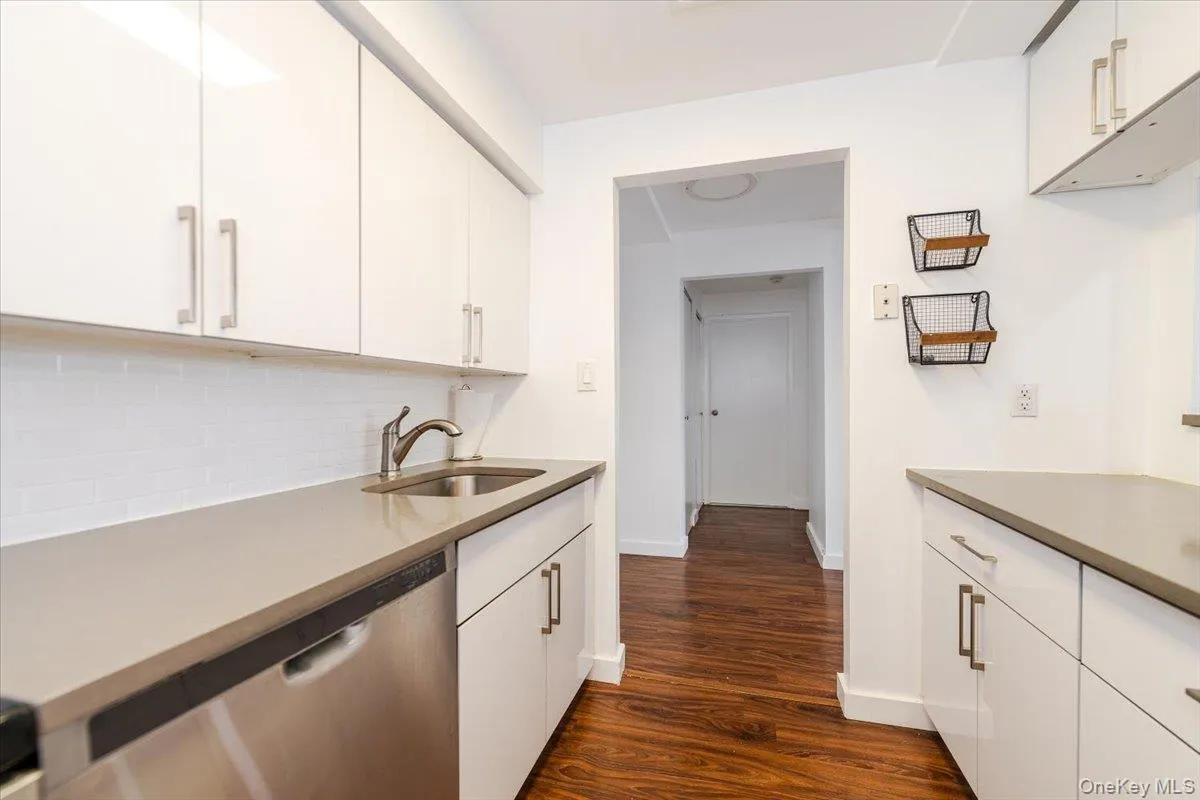 Kitchen featuring dishwasher, decorative backsplash, dark wood-type flooring, and white cabinetry Kitchen featuring dishwasher, decorative backsplash, dark wood-type flooring, and white cabinetry