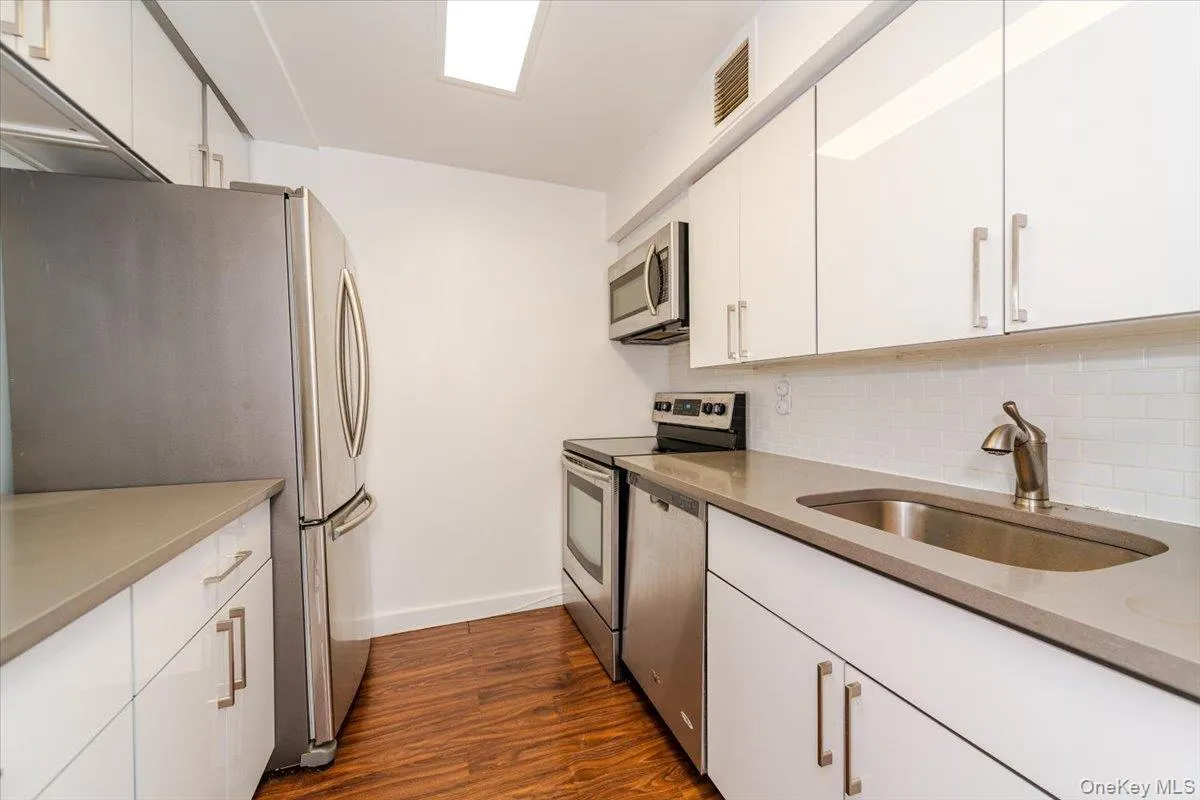 Kitchen featuring stainless steel appliances, backsplash, dark wood-style floors, and white cabinets Kitchen featuring stainless steel appliances, backsplash, dark wood-style floors, and white cabinets