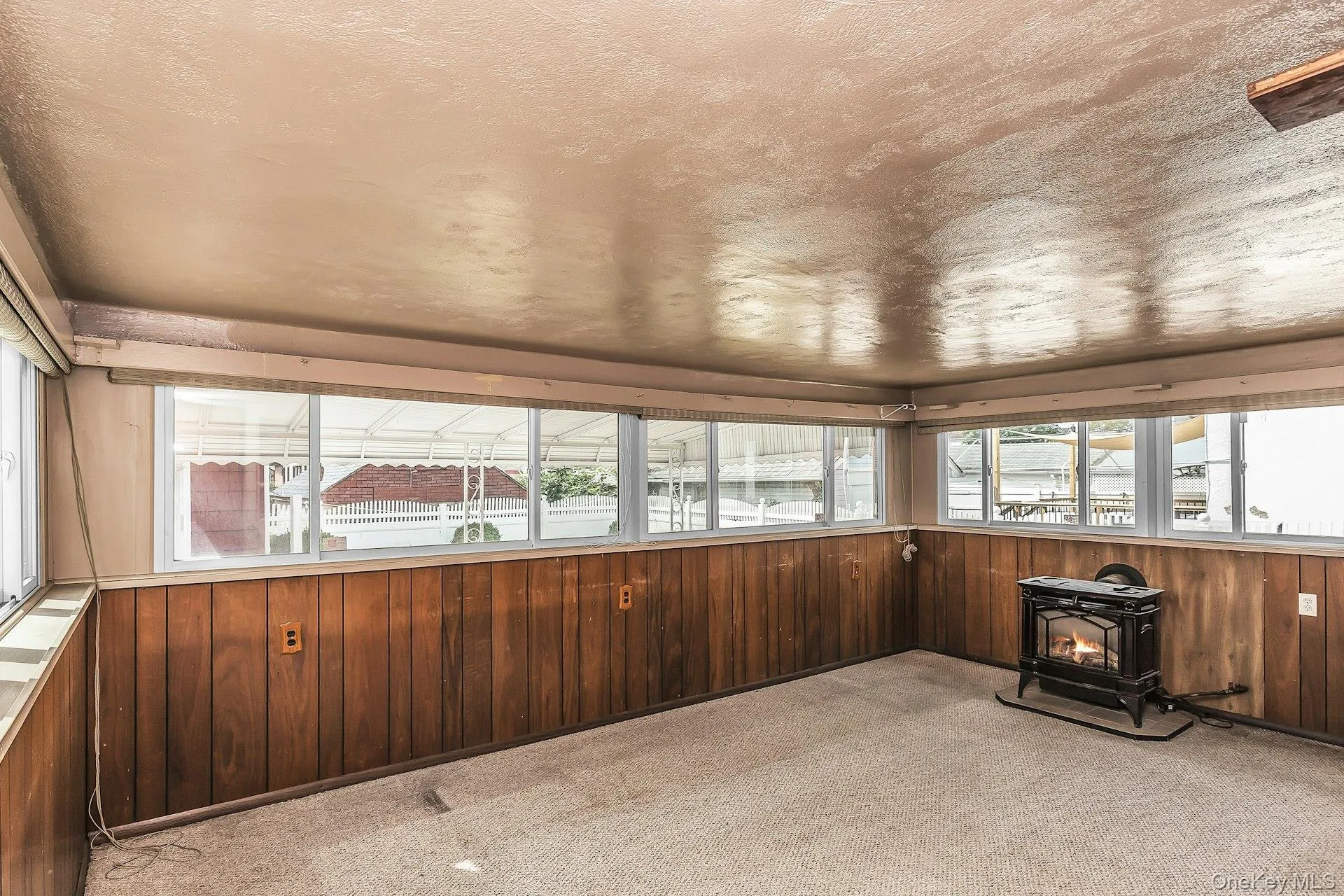 Room featuring wood paneling, multiple windows, and a black cast iron stove Room featuring wood paneling, multiple windows, and a black cast iron stove
