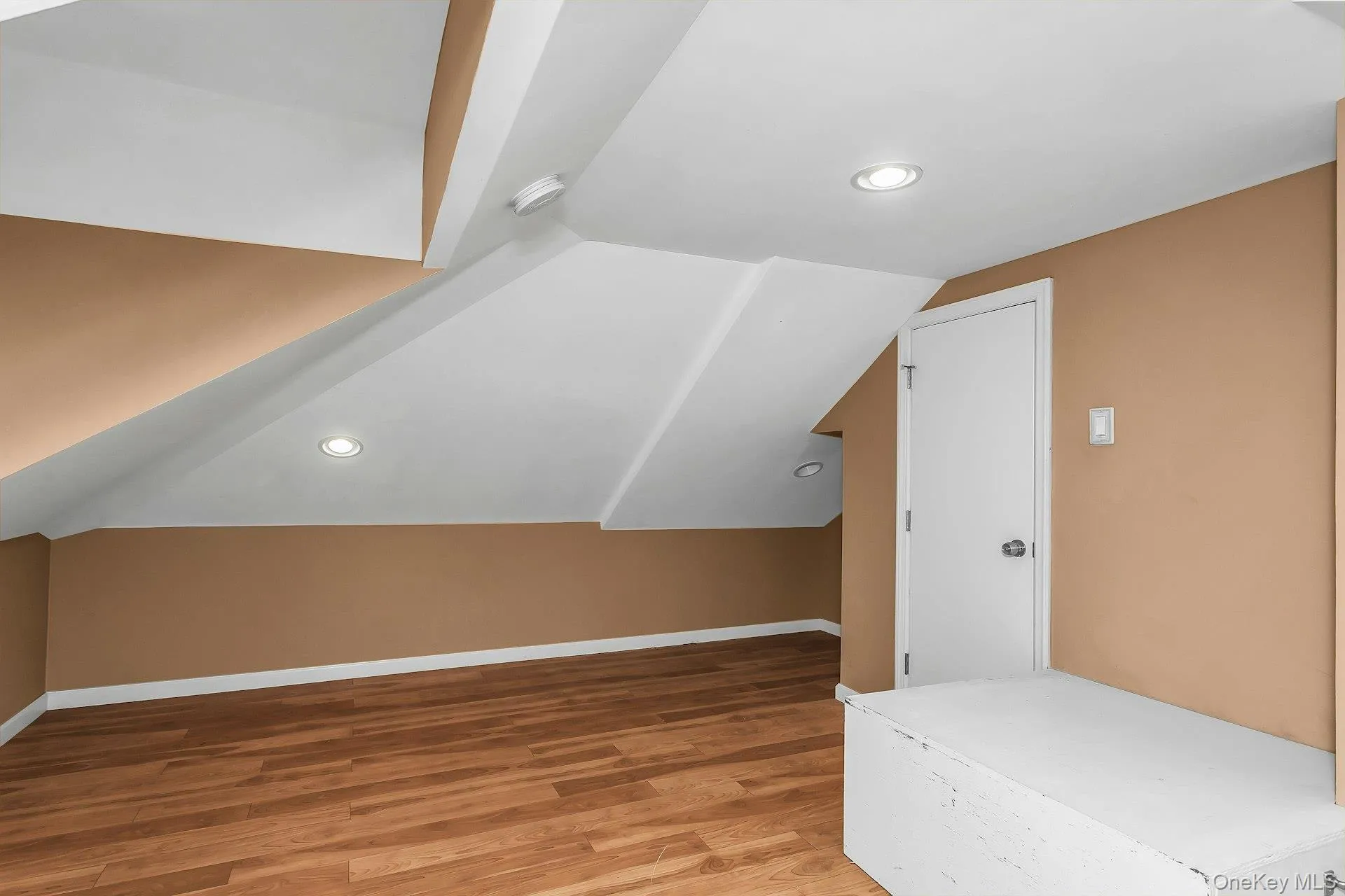 Wood-finish flooring, recessed lighting, neutral wall tones, and an interior door Wood-finish flooring, recessed lighting, neutral wall tones, and an interior door