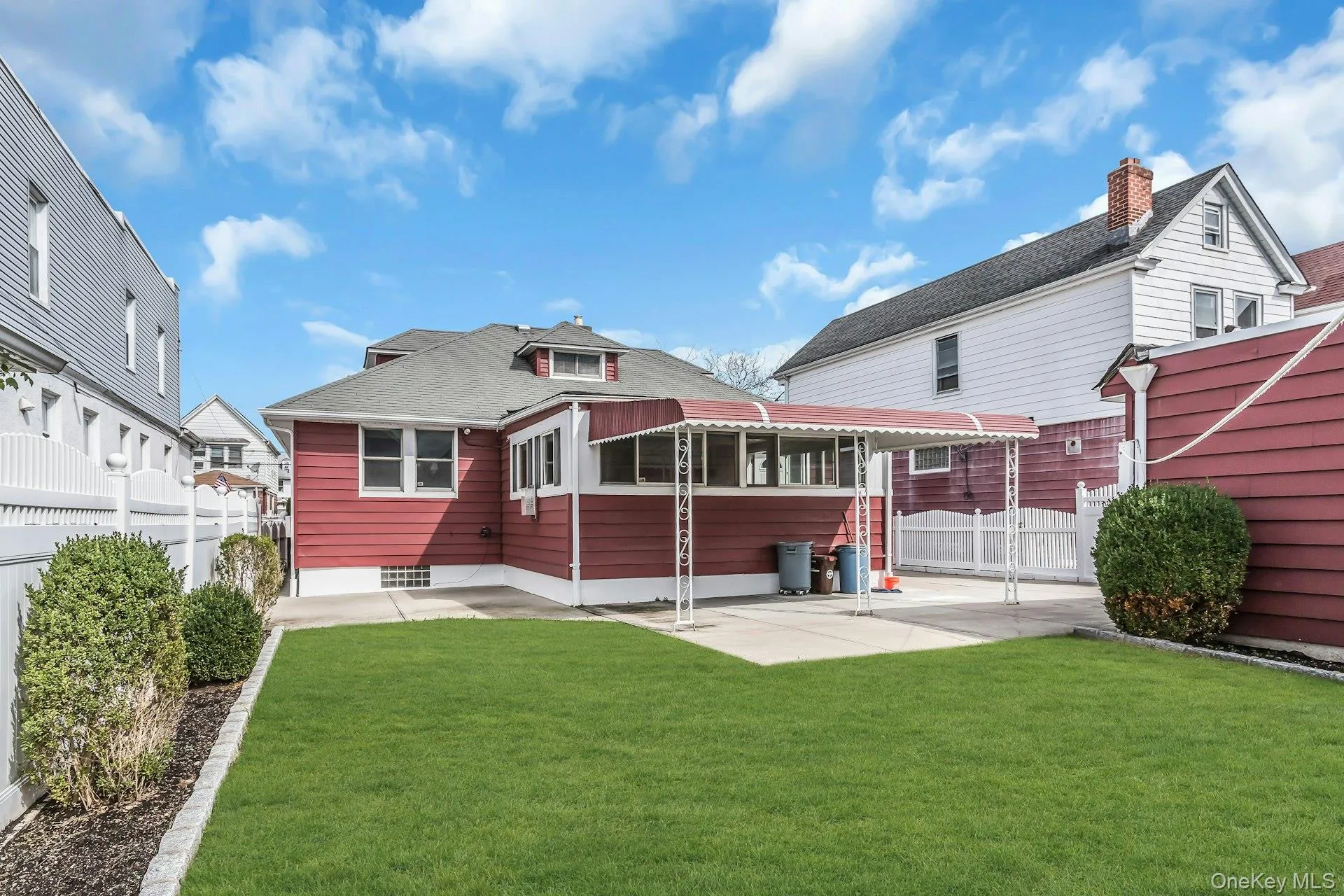 Manicured lawn, mature shrubs, white picket fence, covered patio, and red siding Manicured lawn, mature shrubs, white picket fence, covered patio, and red siding