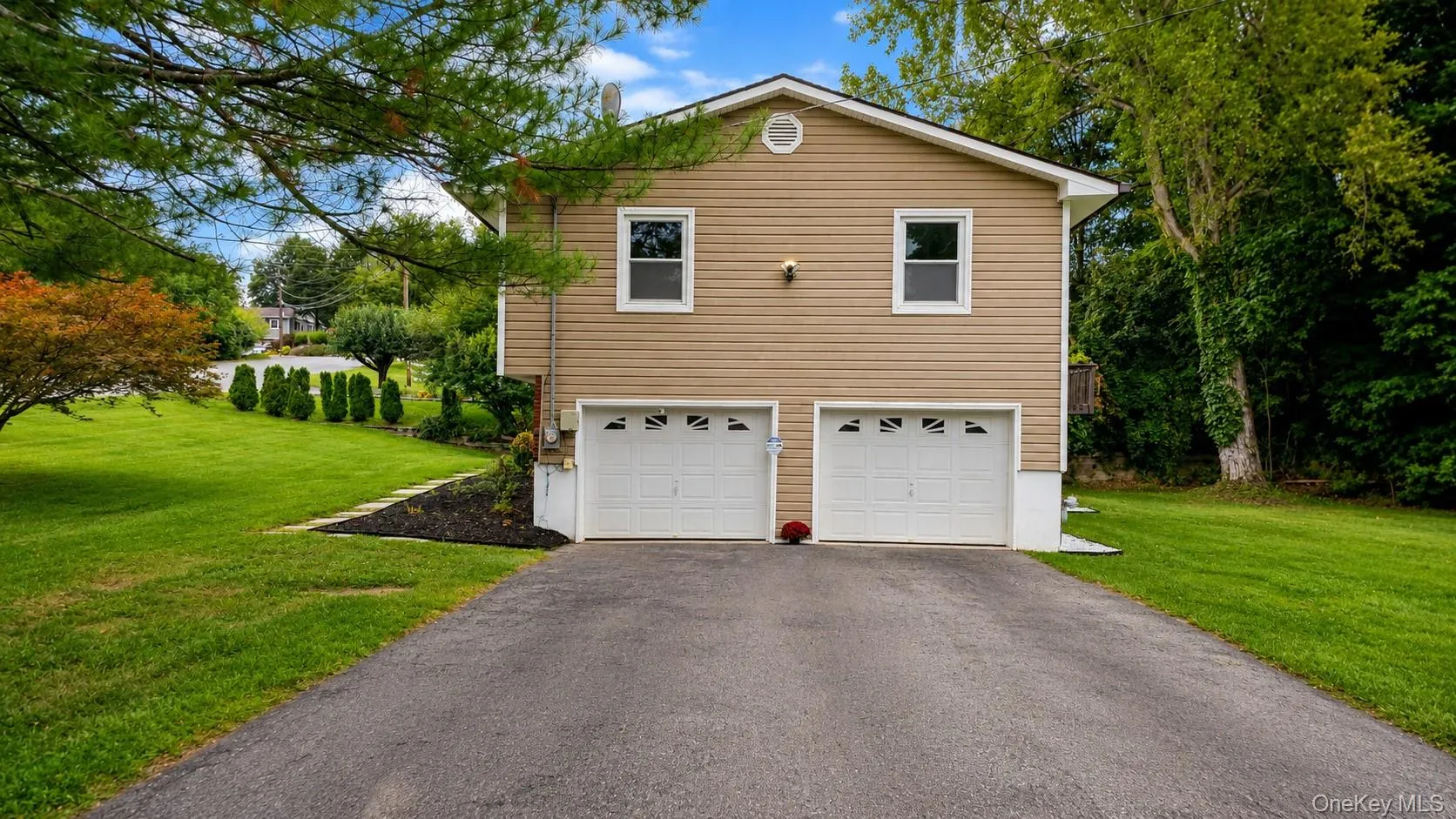 Beige siding exterior, two-car garage, asphalt driveway, mature landscaping, and green lawn Beige siding exterior, two-car garage, asphalt driveway, mature landscaping, and green lawn