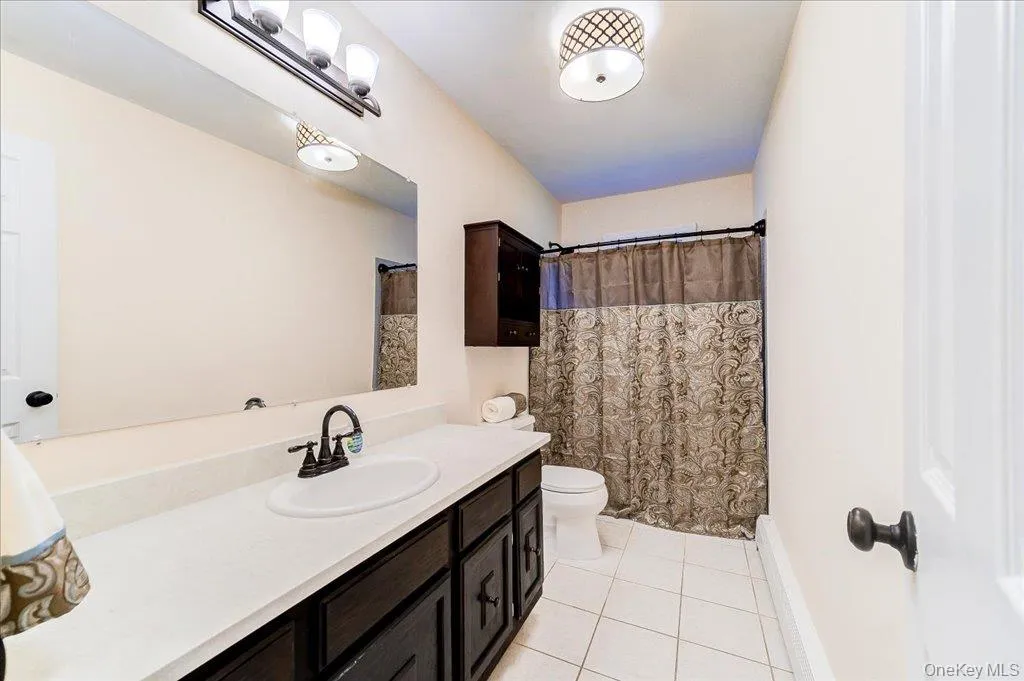 Bathroom featuring a dark wood finish vanity with a solid surface countertop, white ceramic tile flooring, and a built-in wall cabinet Bathroom featuring a dark wood finish vanity with a solid surface countertop, white ceramic tile flooring, and a built-in wall cabinet