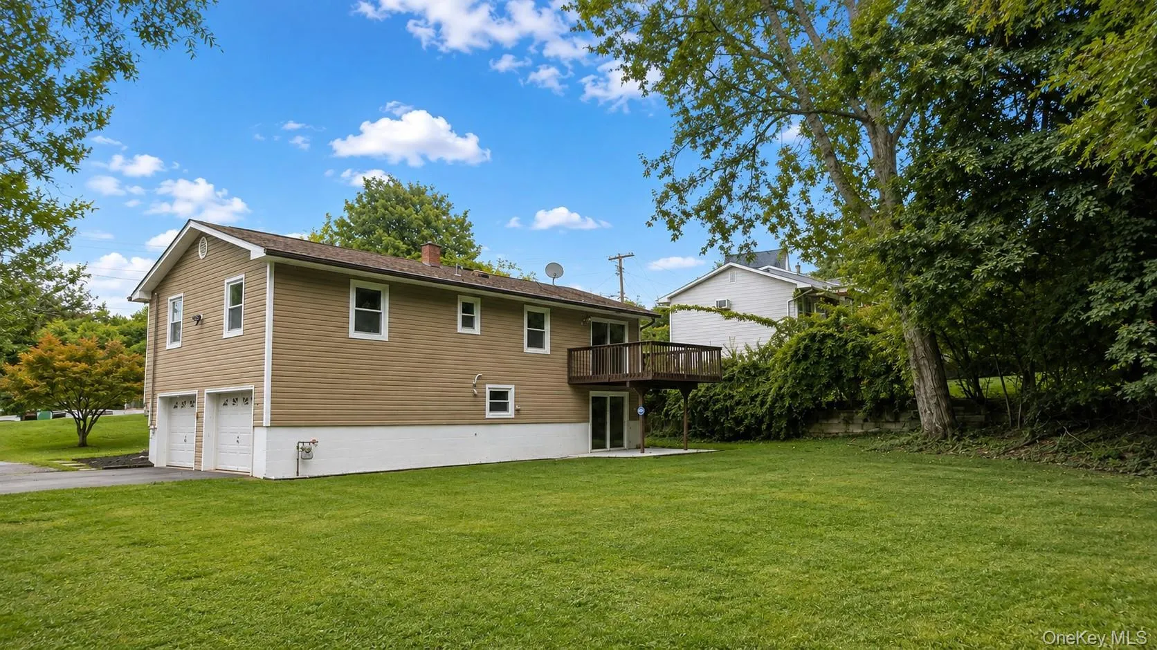 Expansive rear yard featuring a large wooden deck, lower-level patio, and attached two-car garage Expansive rear yard featuring a large wooden deck, lower-level patio, and attached two-car garage