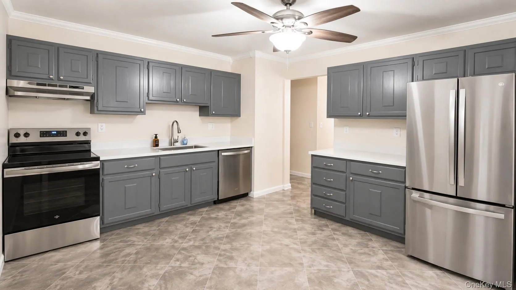Kitchen featuring gray shaker-style cabinetry, white countertops, stainless steel appliances, and a ceiling fan with integrated lighting Kitchen featuring gray shaker-style cabinetry, white countertops, stainless steel appliances, and a ceiling fan with integrated lighting