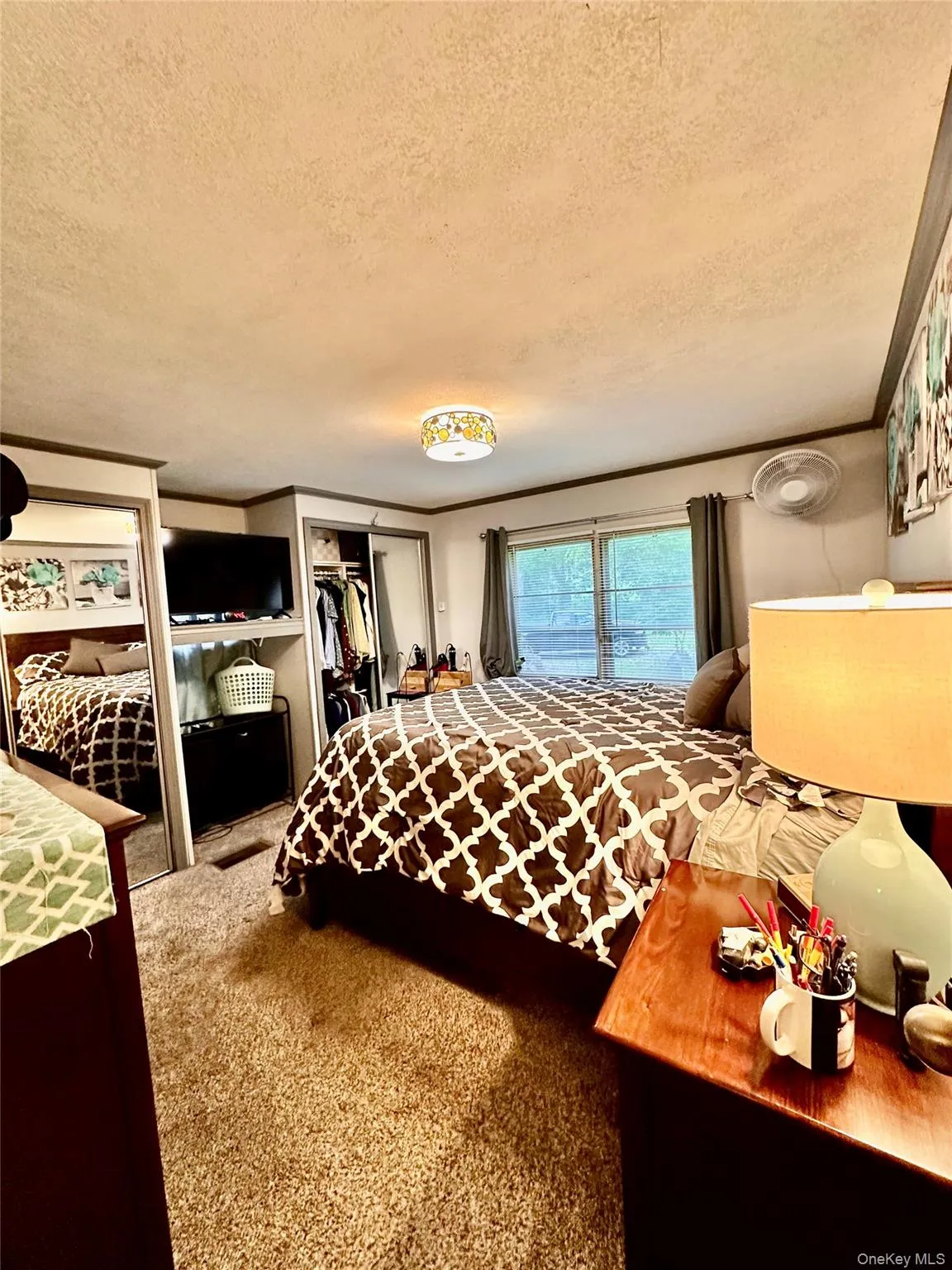 Primary bedroom measuring 12'5" x 12'10" with wall-to-wall carpeting, dual windows with dark-toned drapes, a ceiling-mounted light fixture, and dark wood trim. Primary bedroom measuring 12'5" x 12'10" with wall-to-wall carpeting, dual windows with dark-toned drapes, a ceiling-mounted light fixture, and dark wood trim.