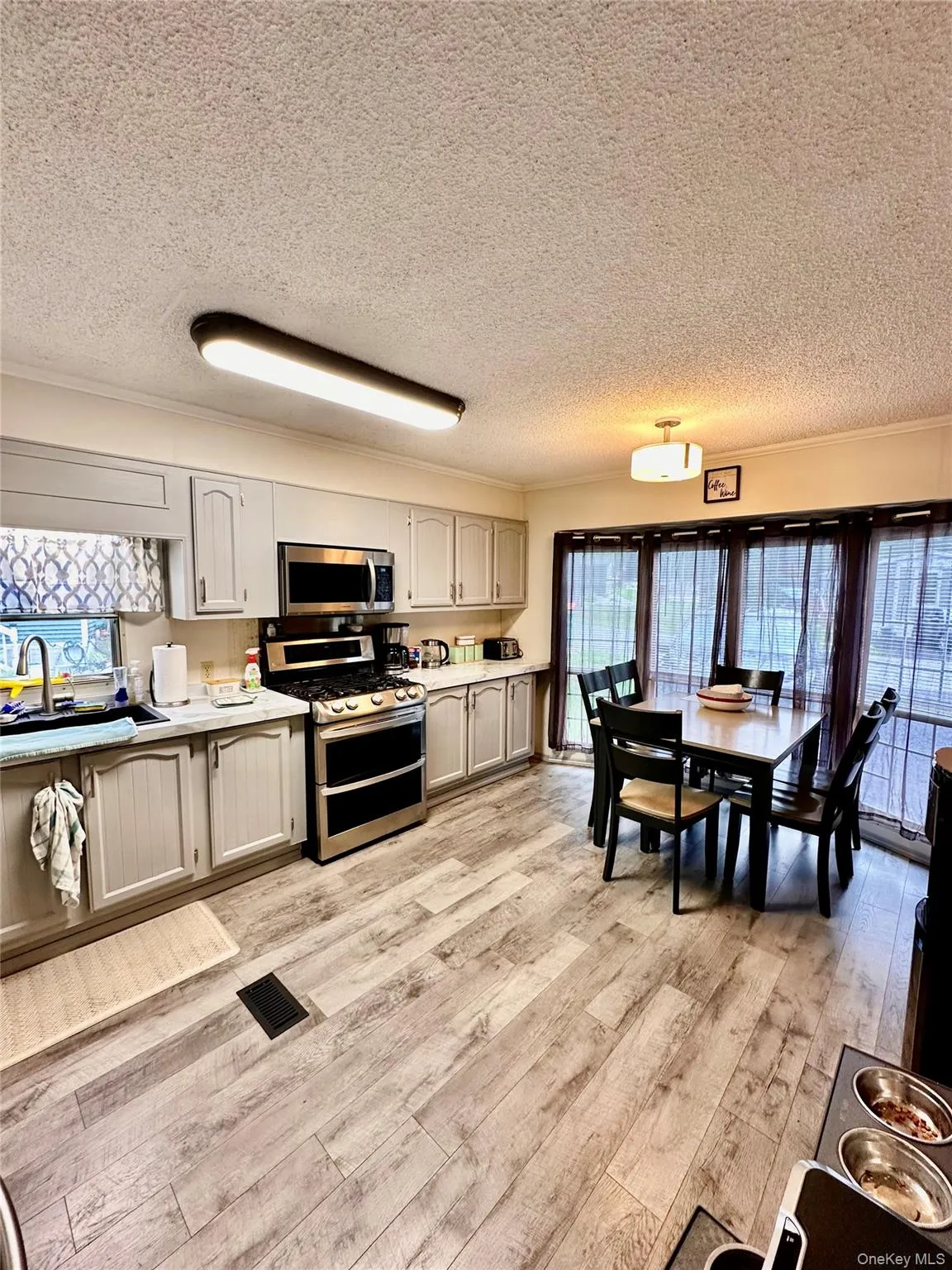 Kitchen featuring light-toned cabinetry, stainless steel appliances, wood-finish flooring, and a dining area with multi-pane windows Kitchen featuring light-toned cabinetry, stainless steel appliances, wood-finish flooring, and a dining area with multi-pane windows