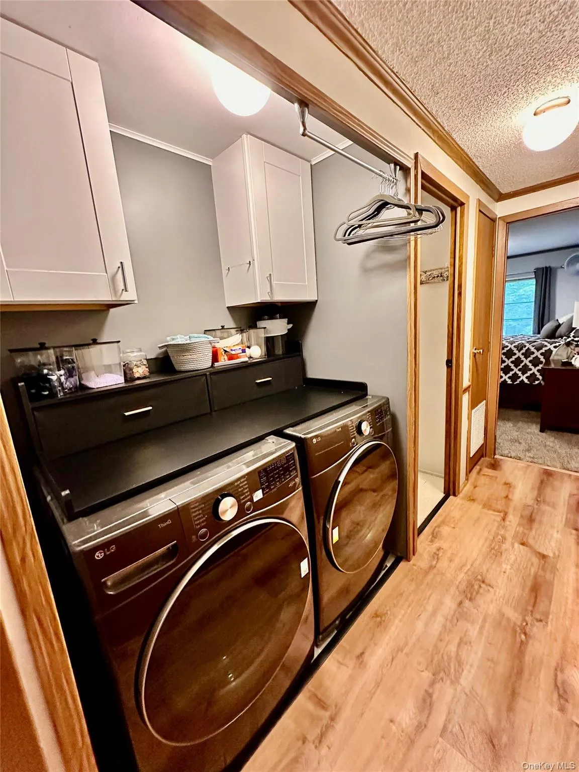 Laundry area featuring overhead cabinetry, wall-mounted hanging rack, and wood-finish flooring - (washer and dryer not included). Laundry area featuring overhead cabinetry, wall-mounted hanging rack, and wood-finish flooring - (washer and dryer not included).