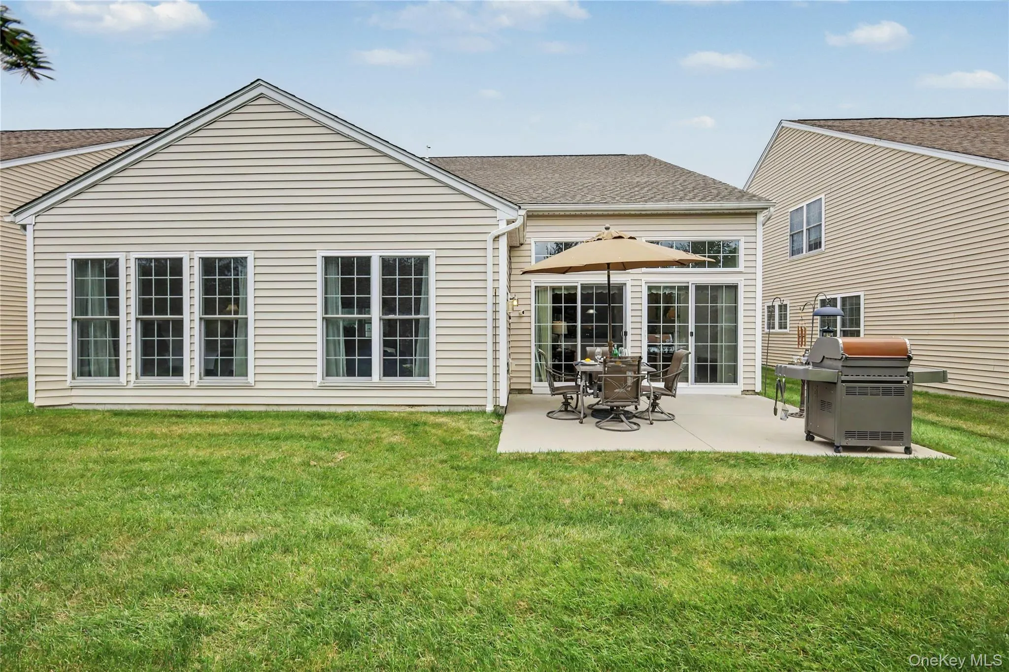 Expansive backyard featuring a concrete patio, multiple windows, and sliding glass doors Expansive backyard featuring a concrete patio, multiple windows, and sliding glass doors