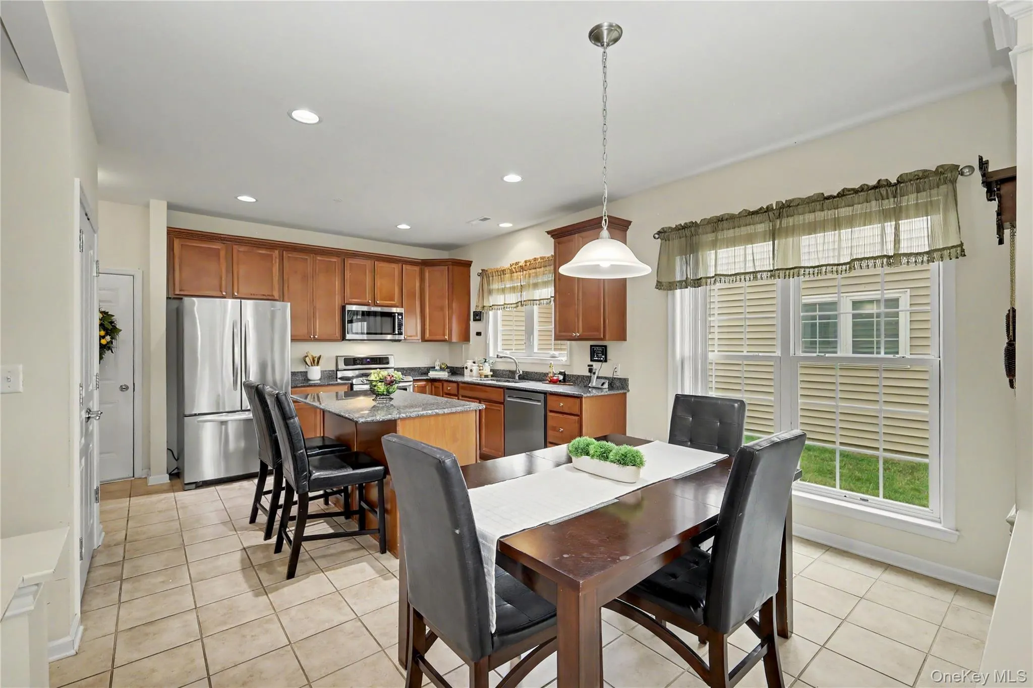 Kitchen featuring wood cabinetry, stainless steel appliances, a center island with a granite countertop, and tile flooring Kitchen featuring wood cabinetry, stainless steel appliances, a center island with a granite countertop, and tile flooring