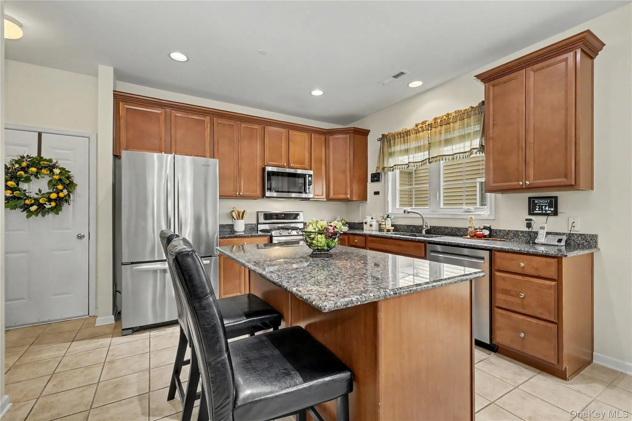 Kitchen featuring tile flooring, wood cabinetry, granite countertops, a center island, and stainless steel appliances Kitchen featuring tile flooring, wood cabinetry, granite countertops, a center island, and stainless steel appliances