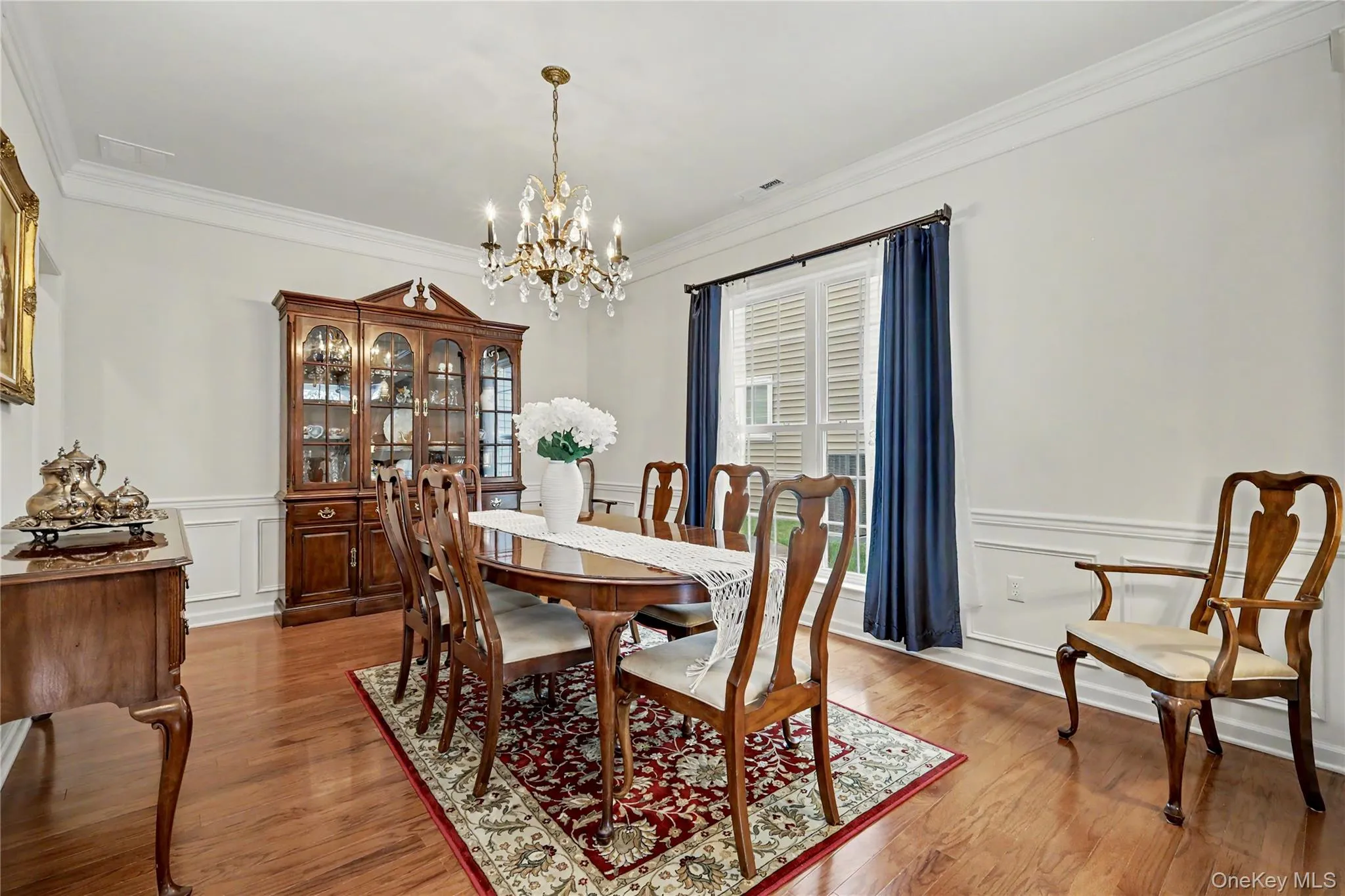 Wood-finish flooring, white wainscoting, crown molding, and a crystal chandelier Wood-finish flooring, white wainscoting, crown molding, and a crystal chandelier