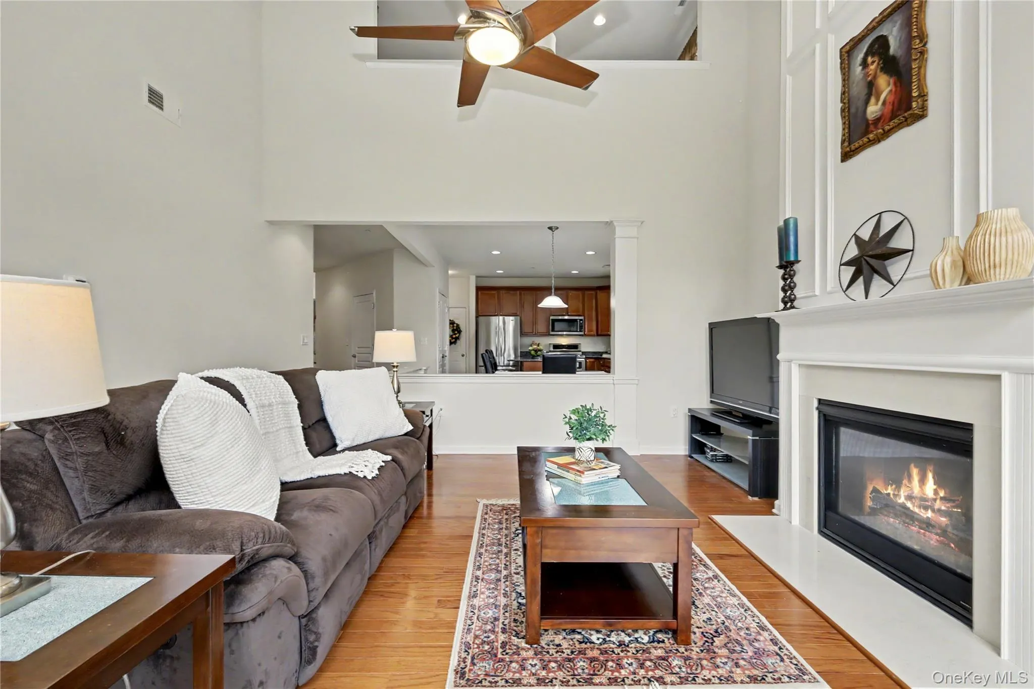 Living area featuring high ceilings, wood-finish flooring, a fireplace with a white mantel, and a ceiling fan Living area featuring high ceilings, wood-finish flooring, a fireplace with a white mantel, and a ceiling fan