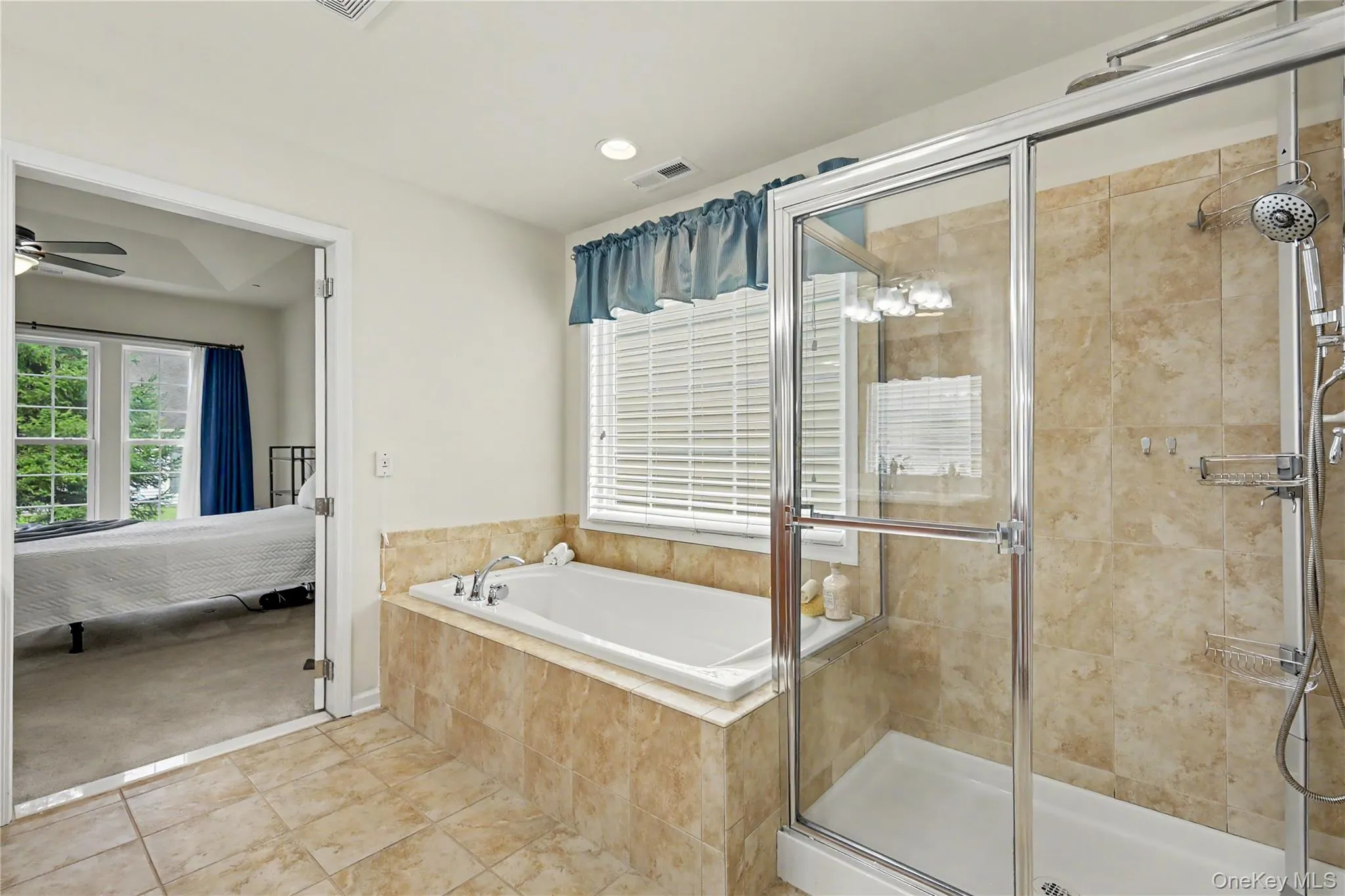 Tiled flooring, built-in bathtub with tiled surround, separate glass-enclosed shower, recessed lighting, and a large window with blinds Tiled flooring, built-in bathtub with tiled surround, separate glass-enclosed shower, recessed lighting, and a large window with blinds