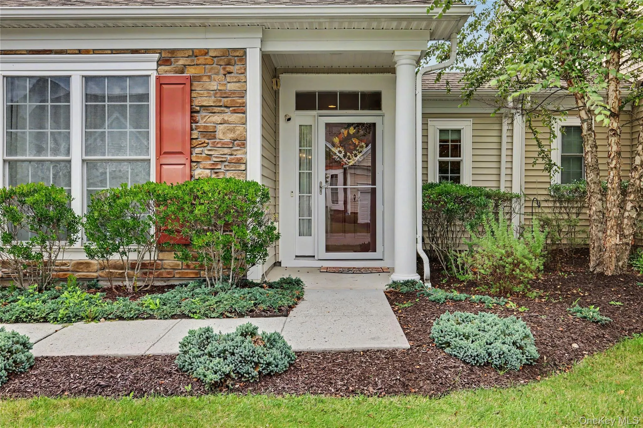 Entryway with stone accents, decorative shutters, a covered porch with a column, and a concrete pathway Entryway with stone accents, decorative shutters, a covered porch with a column, and a concrete pathway