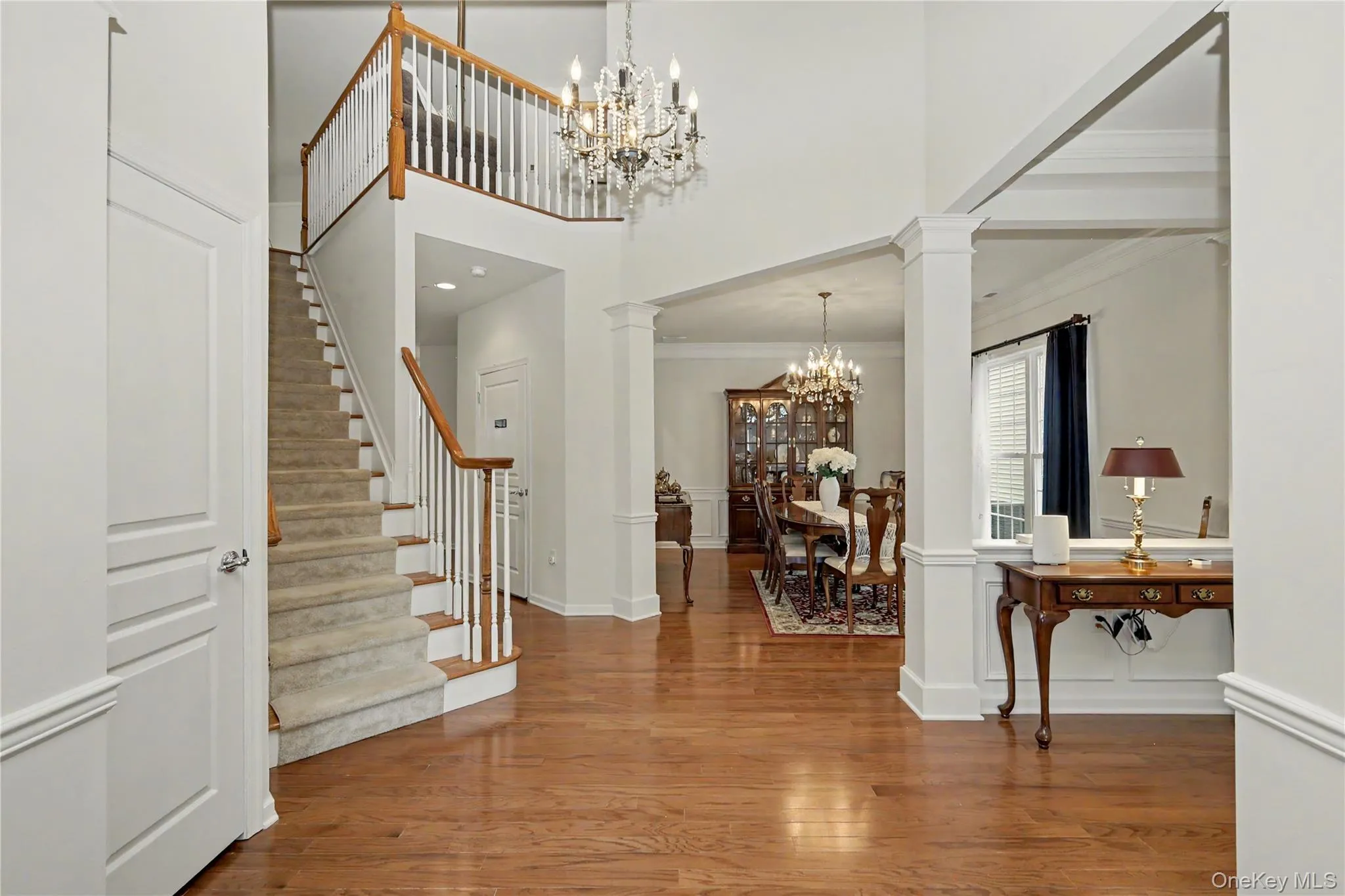 Two-story foyer with wood-finish flooring, a grand staircase, and a crystal chandelier Two-story foyer with wood-finish flooring, a grand staircase, and a crystal chandelier