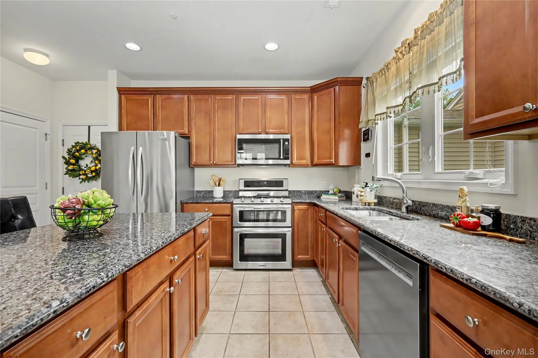Kitchen featuring wood cabinetry, stainless steel appliances, granite countertops, a center island, and tile flooring Kitchen featuring wood cabinetry, stainless steel appliances, granite countertops, a center island, and tile flooring