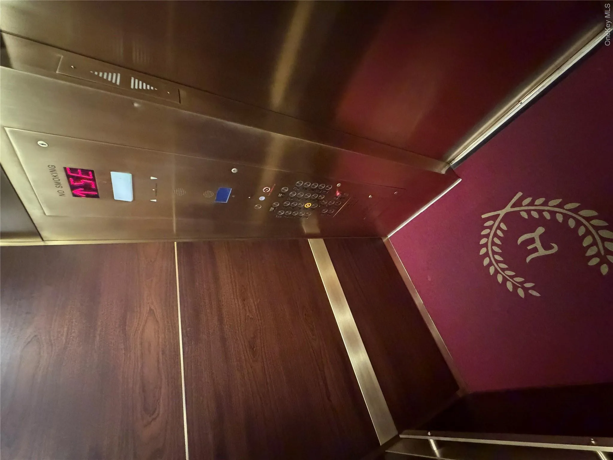 Elevator interior featuring wood-finish wall panels, brass-tone metal accents, and a red patterned floor covering Elevator interior featuring wood-finish wall panels, brass-tone metal accents, and a red patterned floor covering