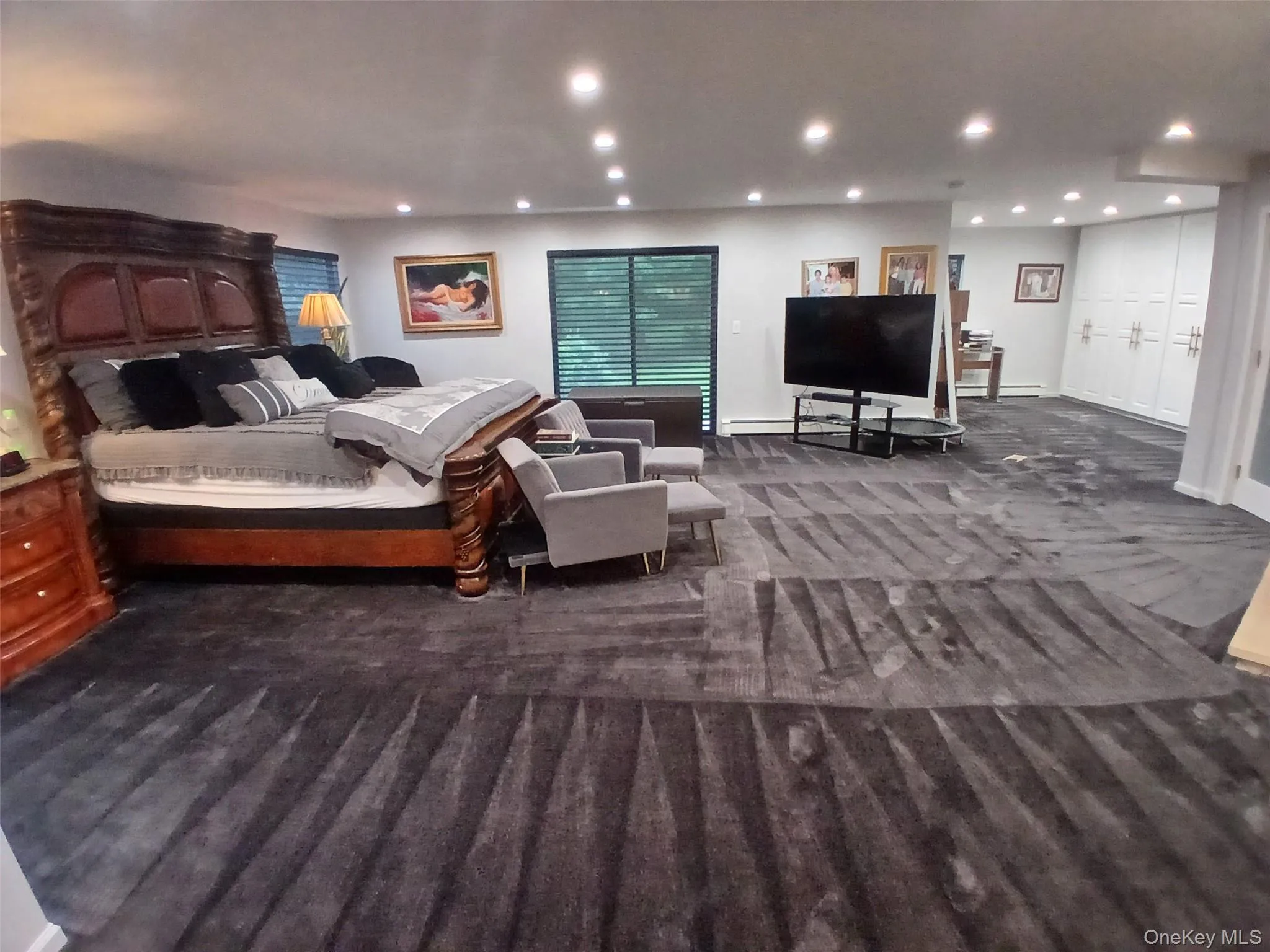 Recessed lighting, dark wood-finish bed frame, built-in cabinetry with panel doors, broad patterned carpeting, and dark window blinds Recessed lighting, dark wood-finish bed frame, built-in cabinetry with panel doors, broad patterned carpeting, and dark window blinds