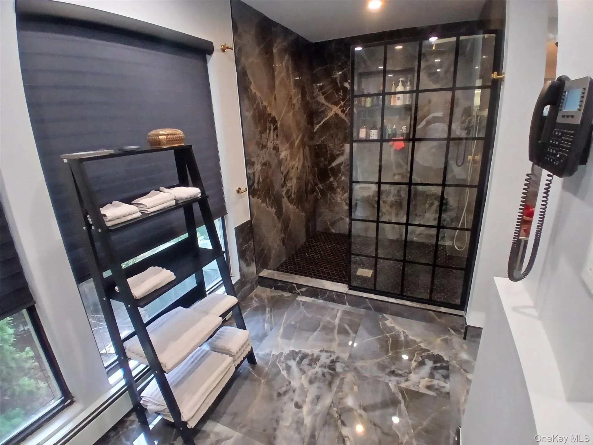 Walk-in shower with grid-patterned glass enclosure, dark-toned marble-look wall tiling, and dark mosaic shower floor Walk-in shower with grid-patterned glass enclosure, dark-toned marble-look wall tiling, and dark mosaic shower floor