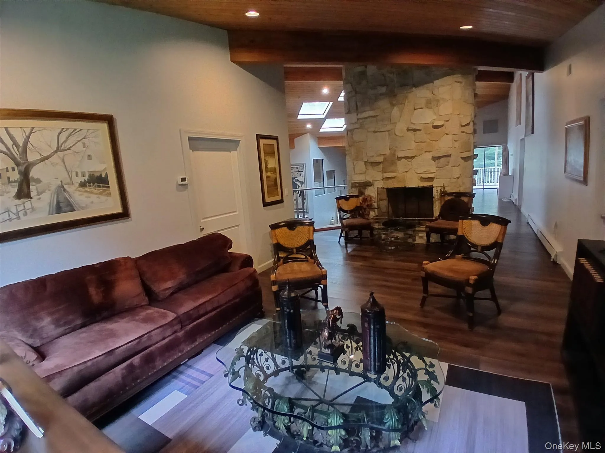 Vaulted wood-beamed ceiling, stone fireplace with hearth, wood-finish flooring, recessed lighting, and multiple skylights Vaulted wood-beamed ceiling, stone fireplace with hearth, wood-finish flooring, recessed lighting, and multiple skylights