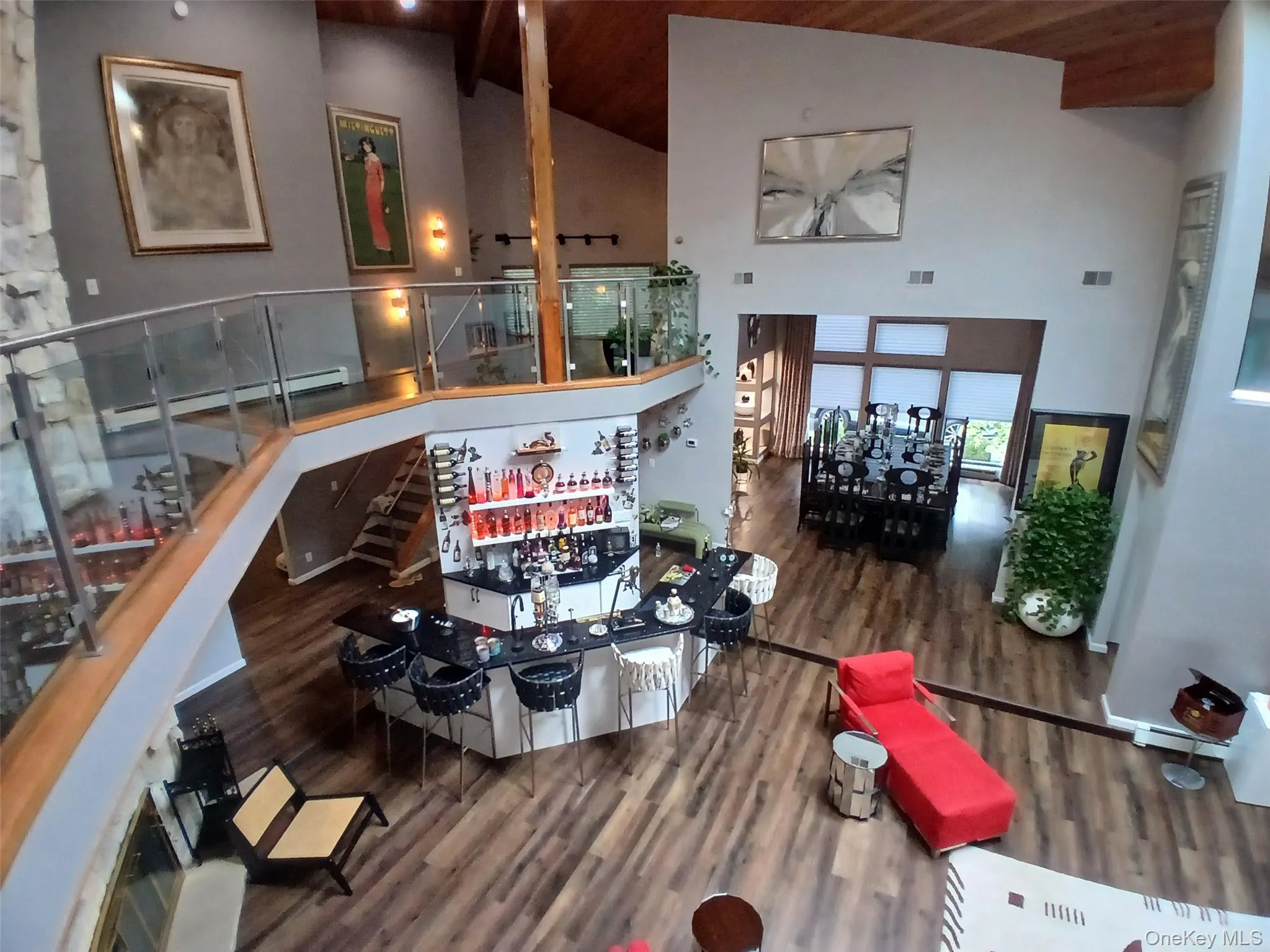 Open-concept living space featuring soaring ceilings with exposed wood beams, a curved mezzanine level with glass railings, and wood-finish flooring throughout Open-concept living space featuring soaring ceilings with exposed wood beams, a curved mezzanine level with glass railings, and wood-finish flooring throughout