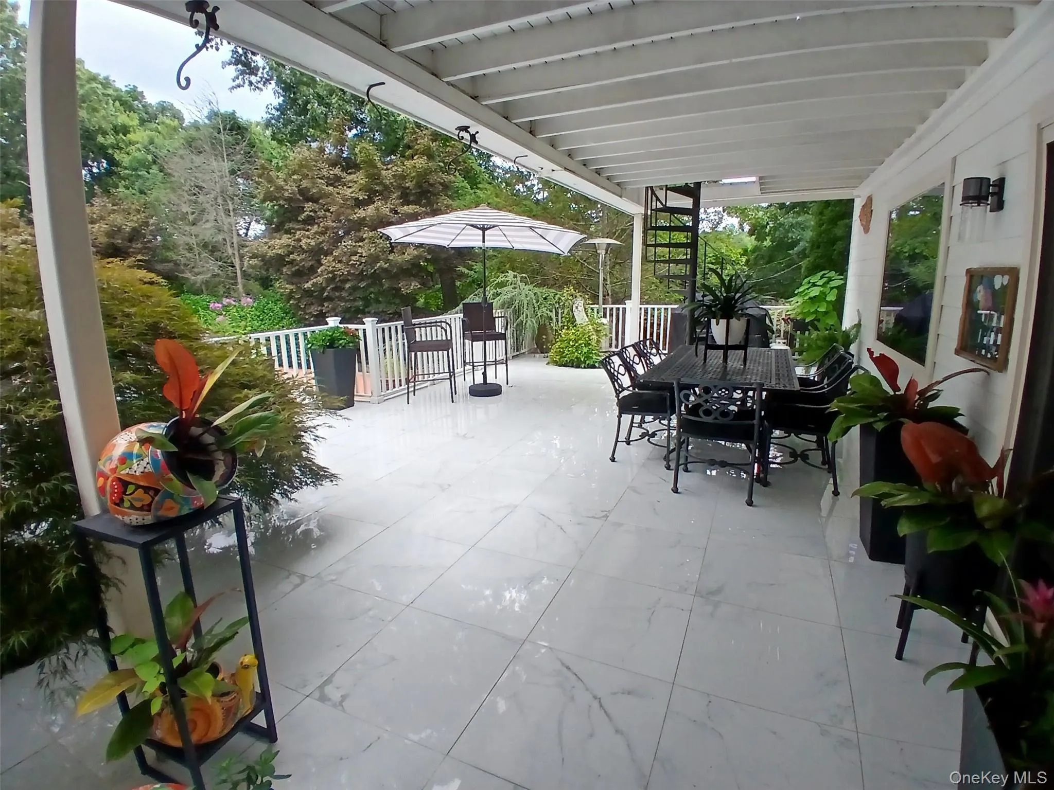 Expansive covered patio featuring large format tile flooring, white railing, and a black spiral staircase Expansive covered patio featuring large format tile flooring, white railing, and a black spiral staircase