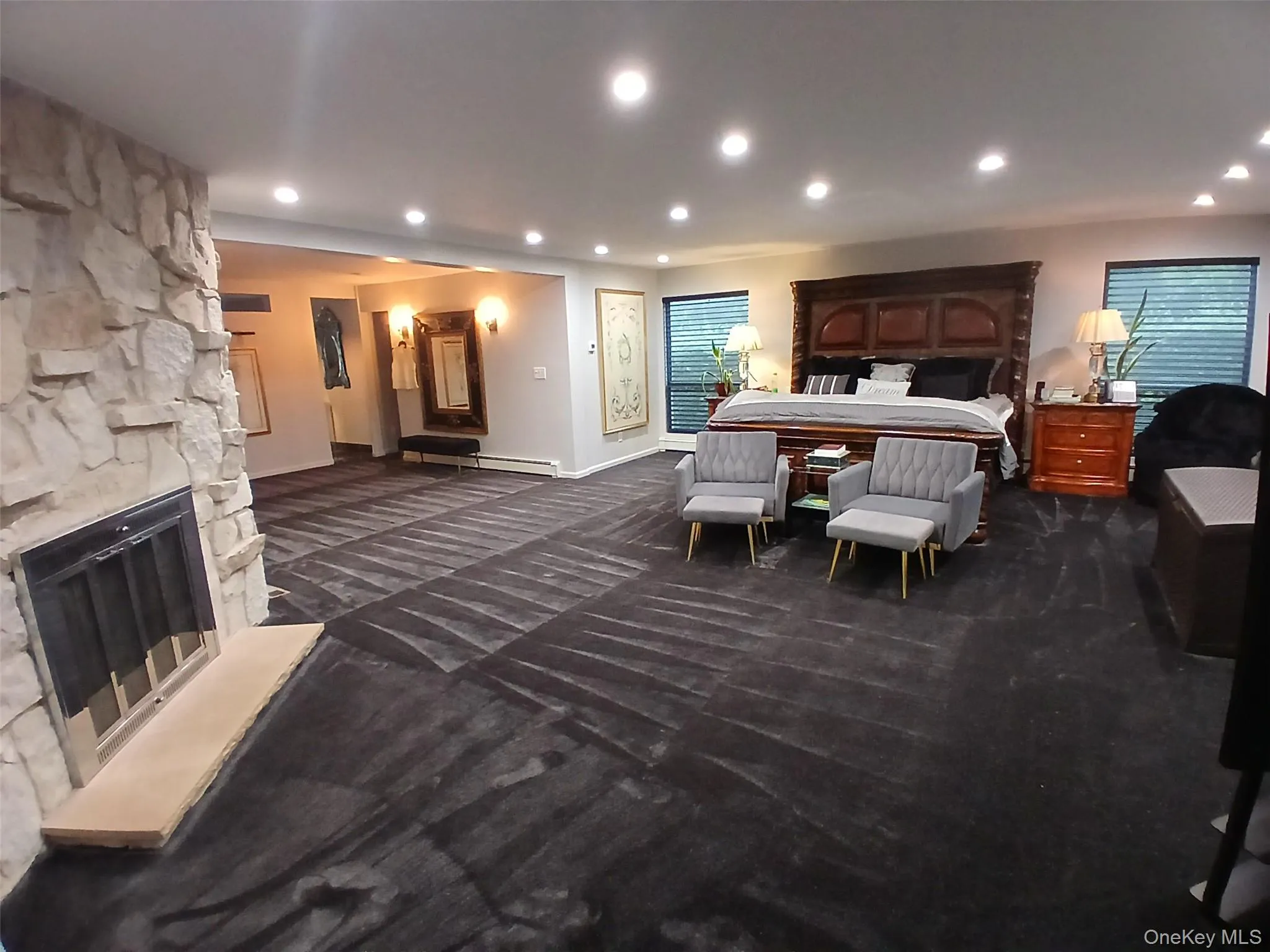 Spacious room featuring a stone-clad fireplace with a hearth, recessed lighting, and multiple windows Spacious room featuring a stone-clad fireplace with a hearth, recessed lighting, and multiple windows