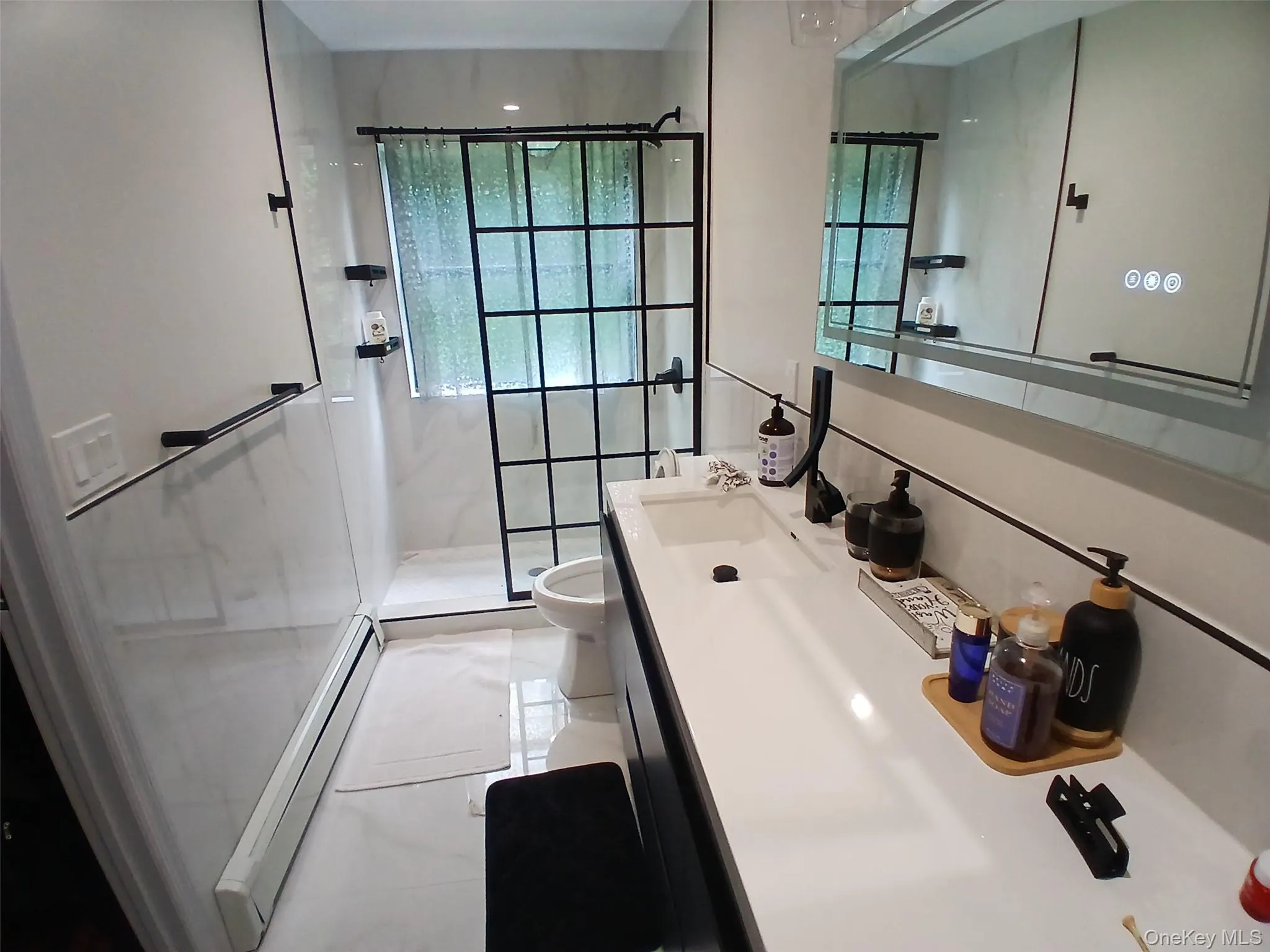 Modern bathroom featuring a walk-in shower with grid-patterned glass enclosure, large format wall and floor tile, an integrated sink vanity, and an illuminated mirrored medicine cabinet Modern bathroom featuring a walk-in shower with grid-patterned glass enclosure, large format wall and floor tile, an integrated sink vanity, and an illuminated mirrored medicine cabinet