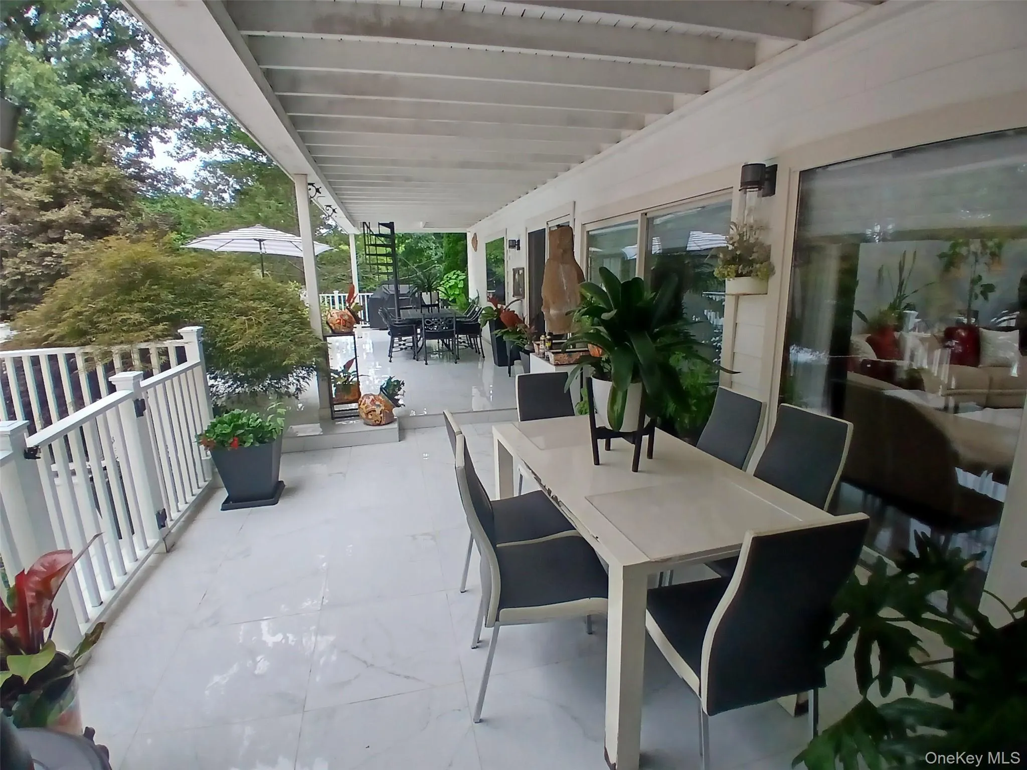 Expansive outdoor patio with a covered pergola, light-toned flooring, white railing, and multiple sliding glass doors Expansive outdoor patio with a covered pergola, light-toned flooring, white railing, and multiple sliding glass doors